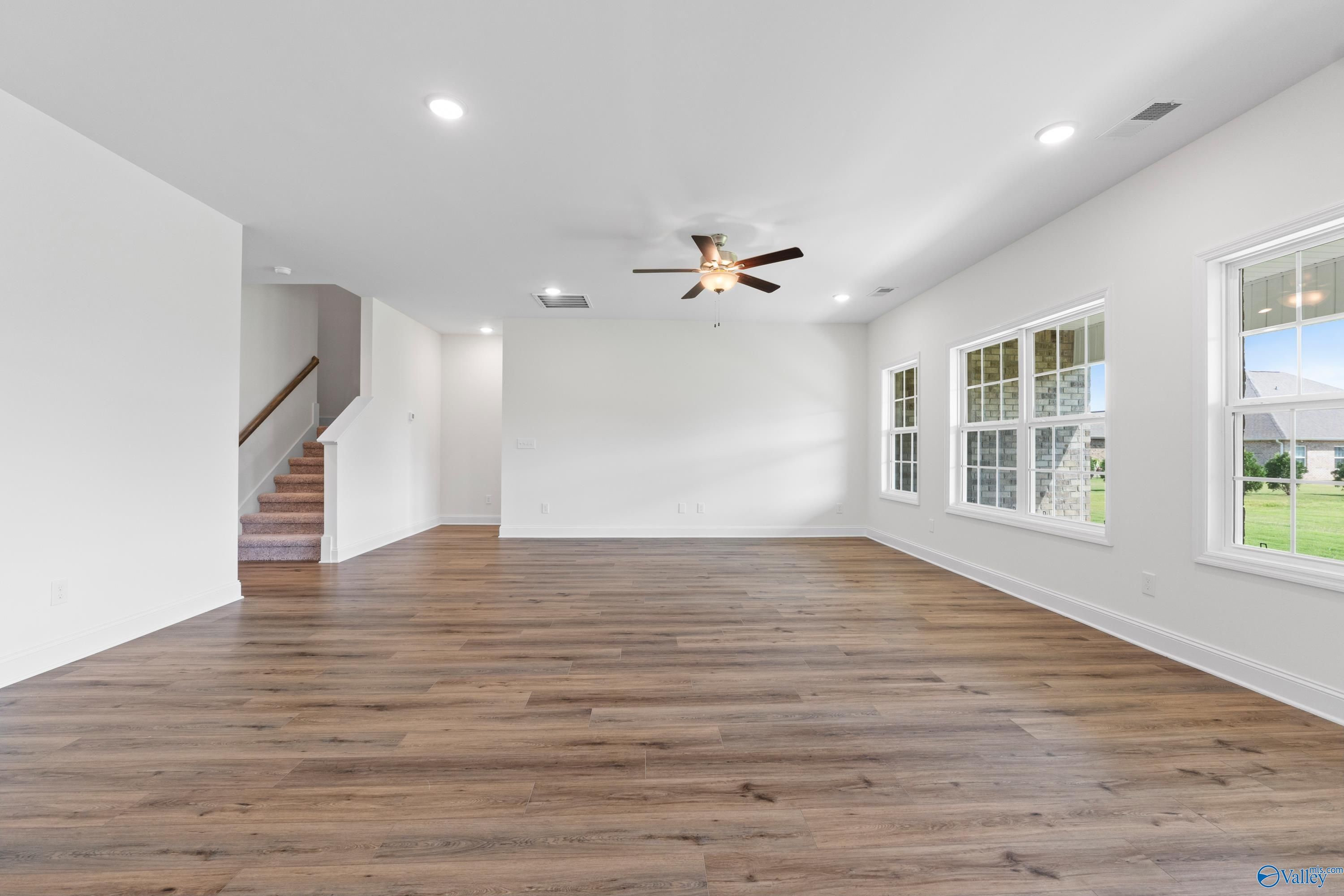 Spacious great room with hardwood floors, dual ceiling fans, large windows, and staircase in Davidson Homes The Rockford B with Bonus, Toney, AL