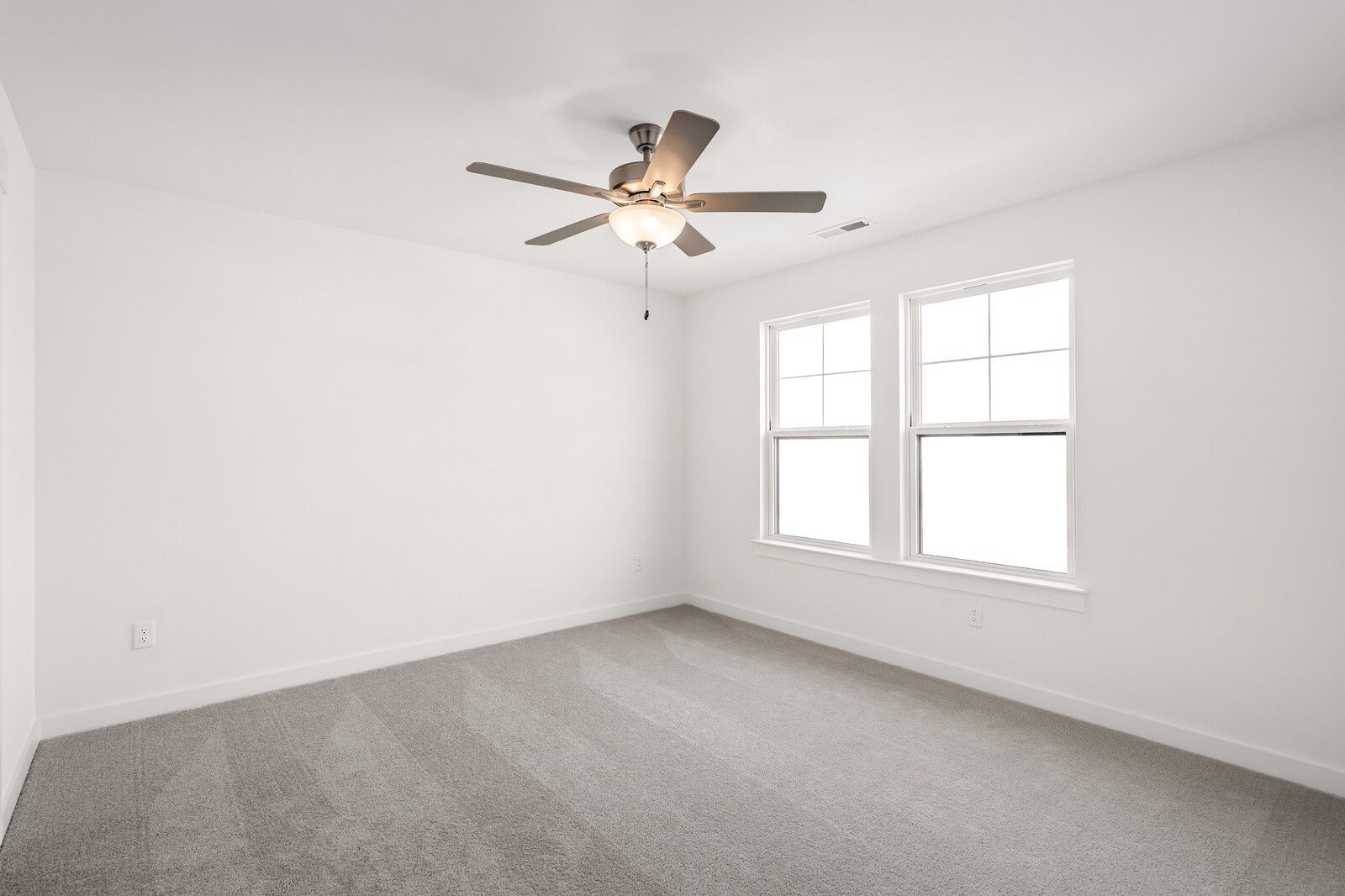 Bright empty bedroom with white walls, gray carpet, dual ceiling fans, and large windows in Davidson Homes Willow D, Mt. Juliet