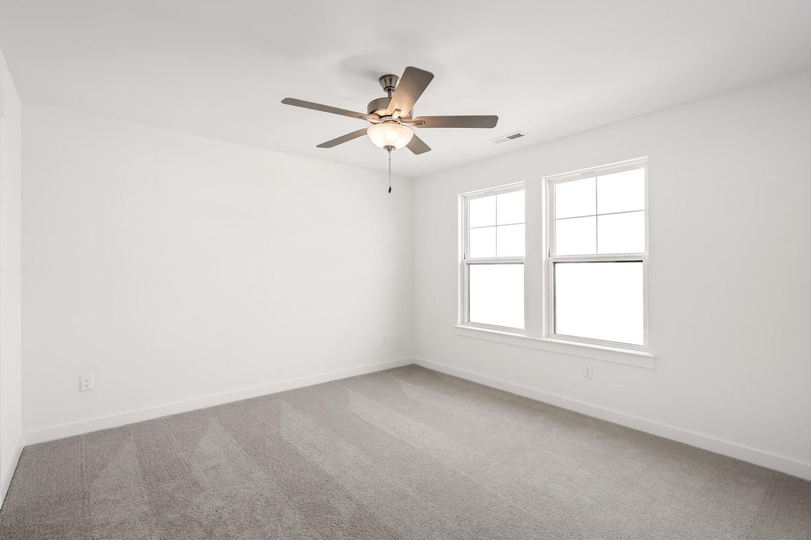 Bright empty bedroom with white walls, gray carpet, dual ceiling fans, and large windows in Davidson Homes Willow D, Mt. Juliet