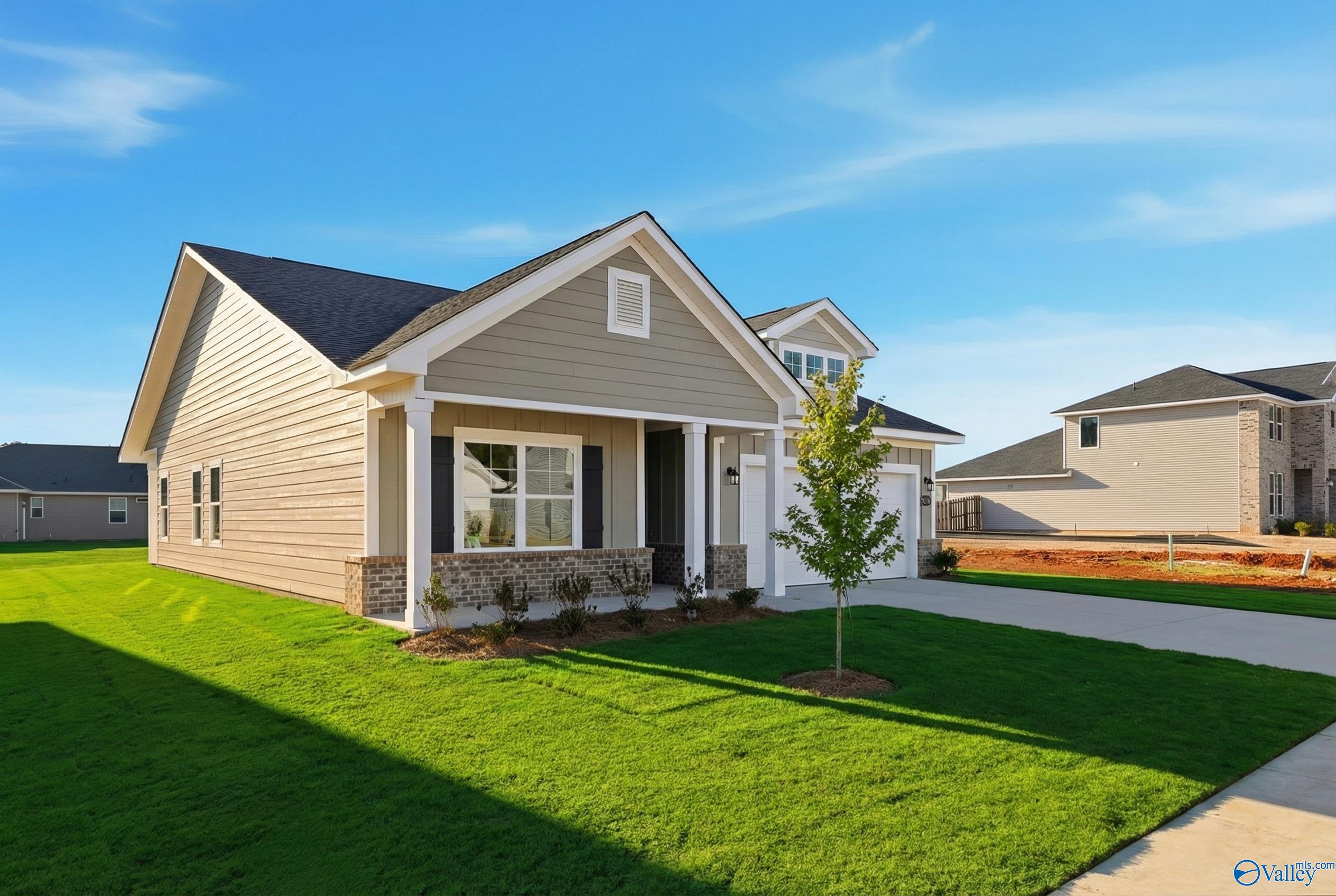 Modern 1-story beige home with gabled roof, covered porch, stone accents, and 2-car garage in Forest Glen, Hazel Green, Alabama