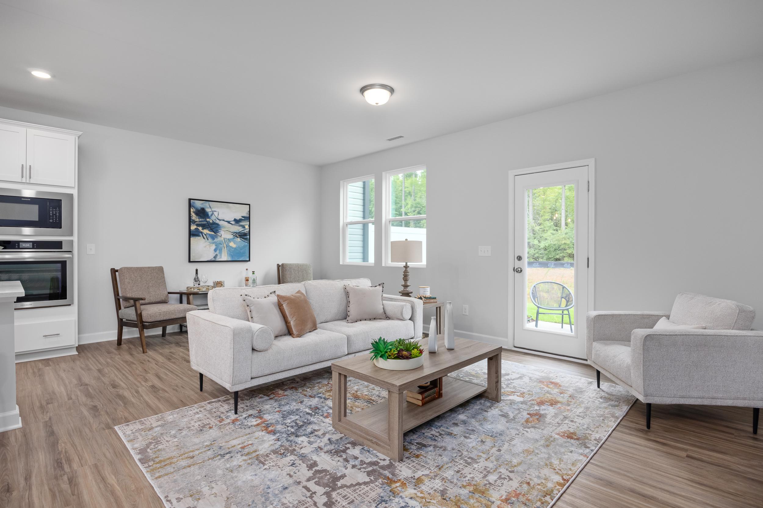 Open-concept living room in The Warren, featuring modern furniture, a patterned area rug, and sleek built-in kitchen wall oven.