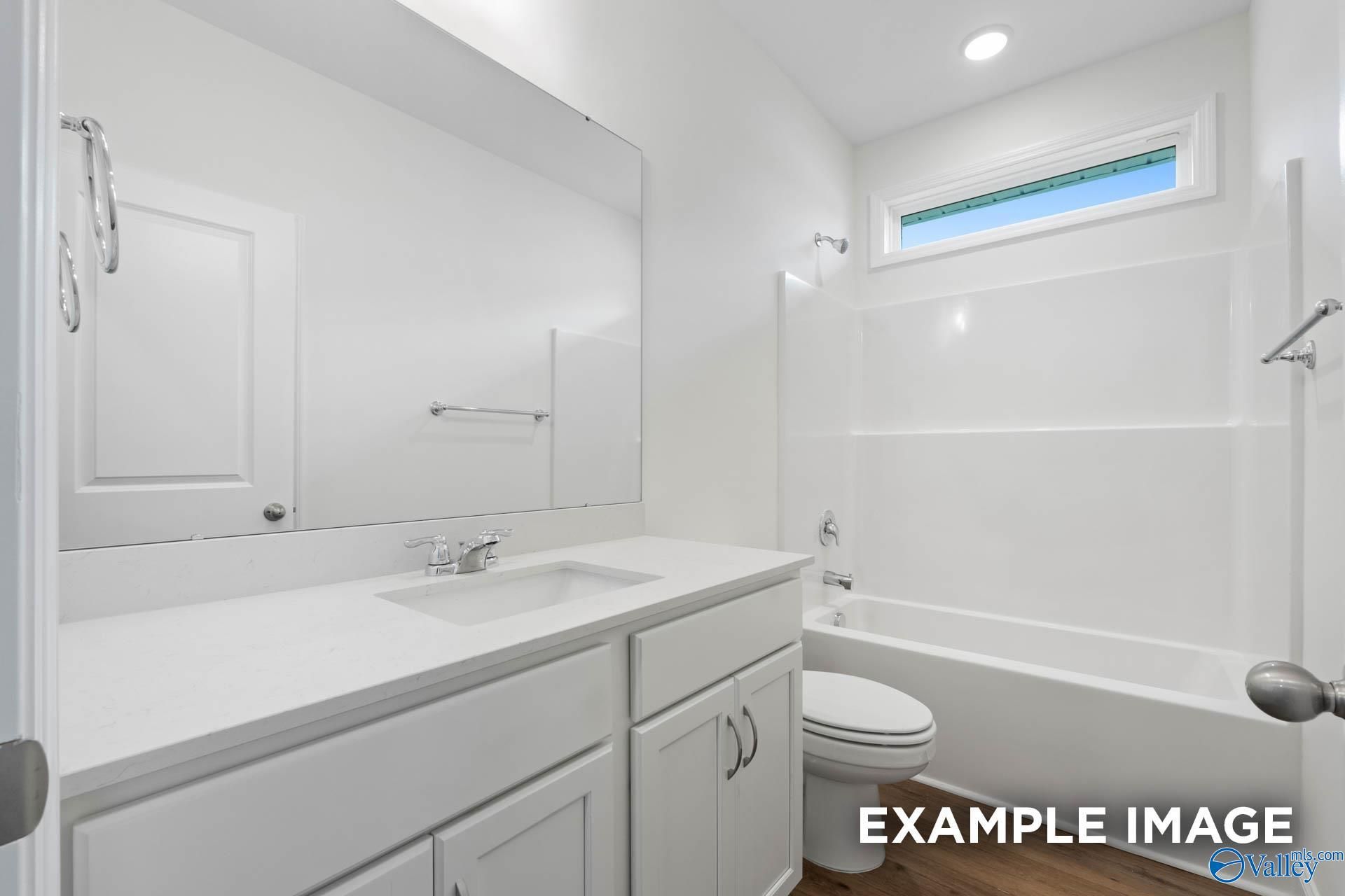 Bright white bathroom with double vanity, soaking tub, and clerestory window in Evermore Homes The Daphne E, Harvest AL