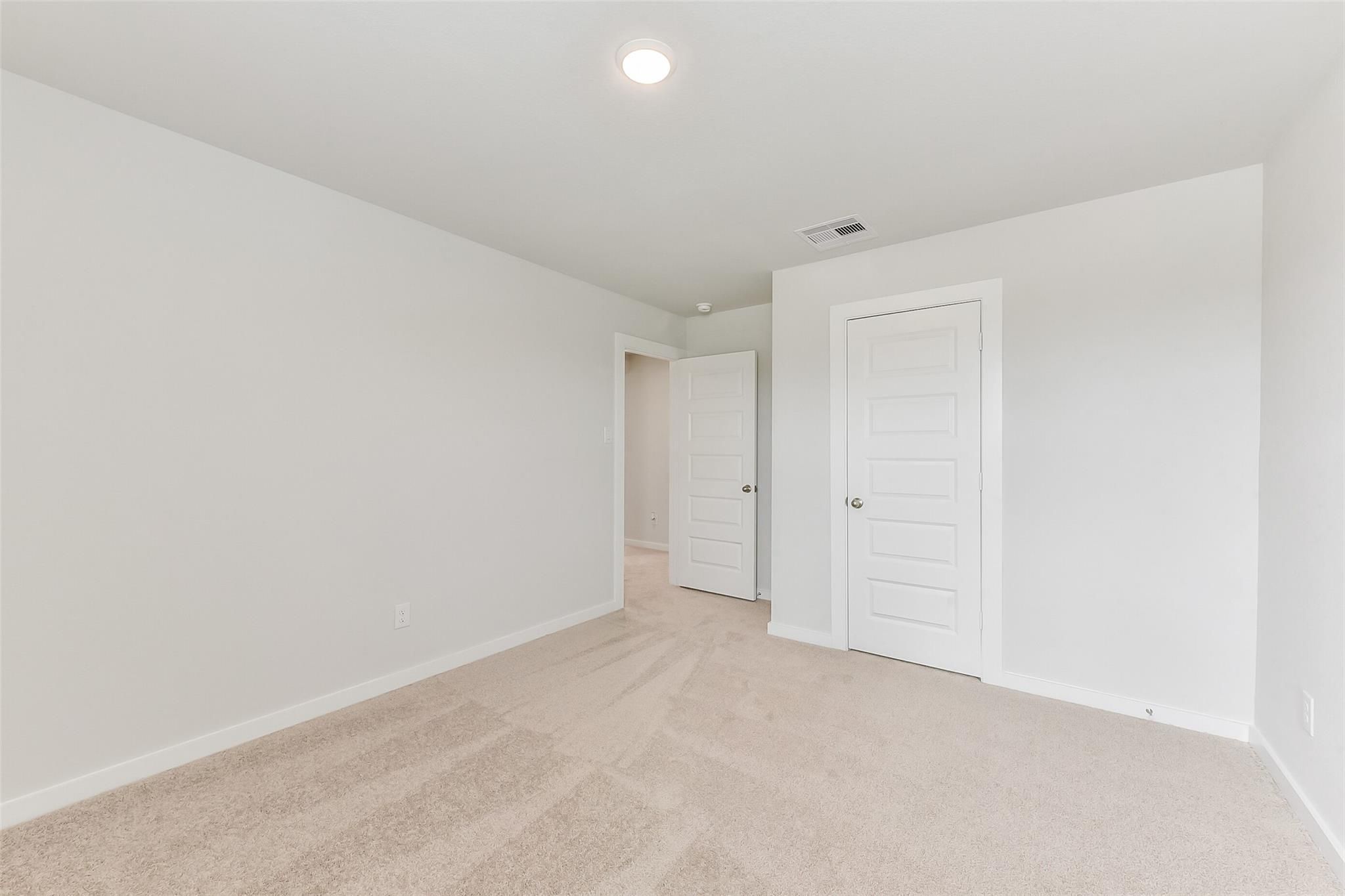 Bright secondary bedroom featuring white walls, beige carpet, open hallway door, and closet in Davidson Homes The Sabine F, Dayton, Texas