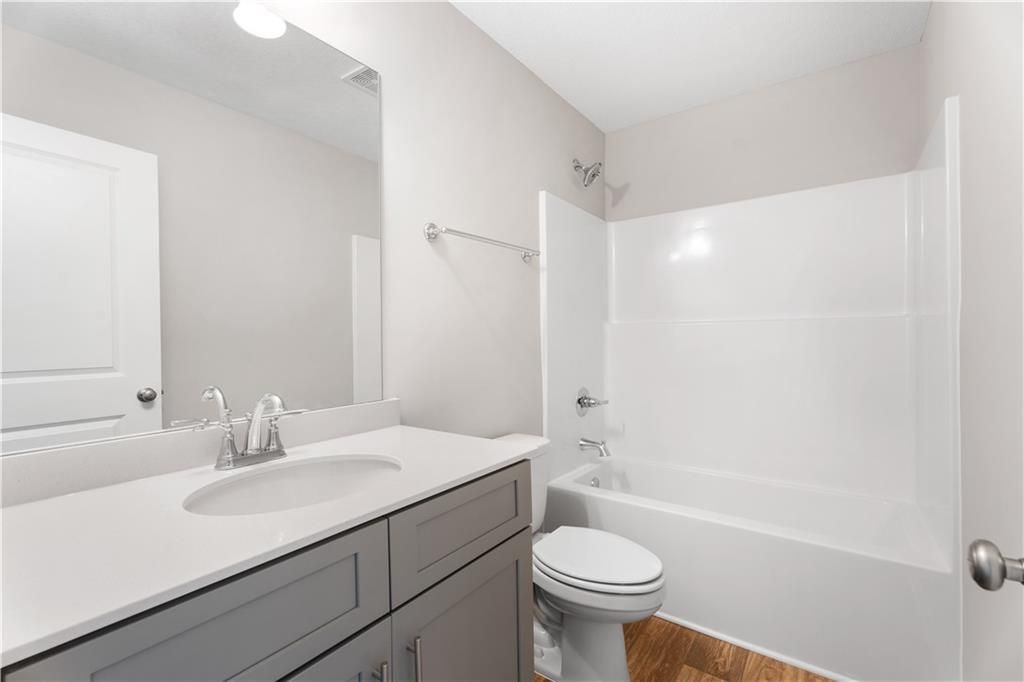 Modern bathroom with white tub-shower combo, gray vanity sink, toilet and wood floors in Davidson Homes The Washington, Phenix City, Alabama