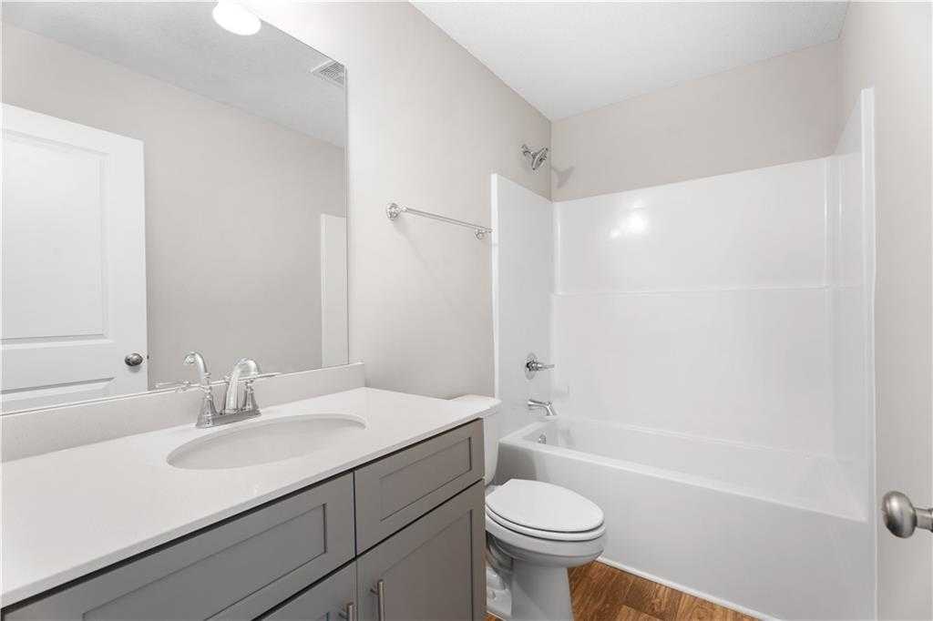 Modern bathroom with white tub-shower combo, gray vanity sink, toilet and wood floors in Davidson Homes The Washington, Phenix City, Alabama