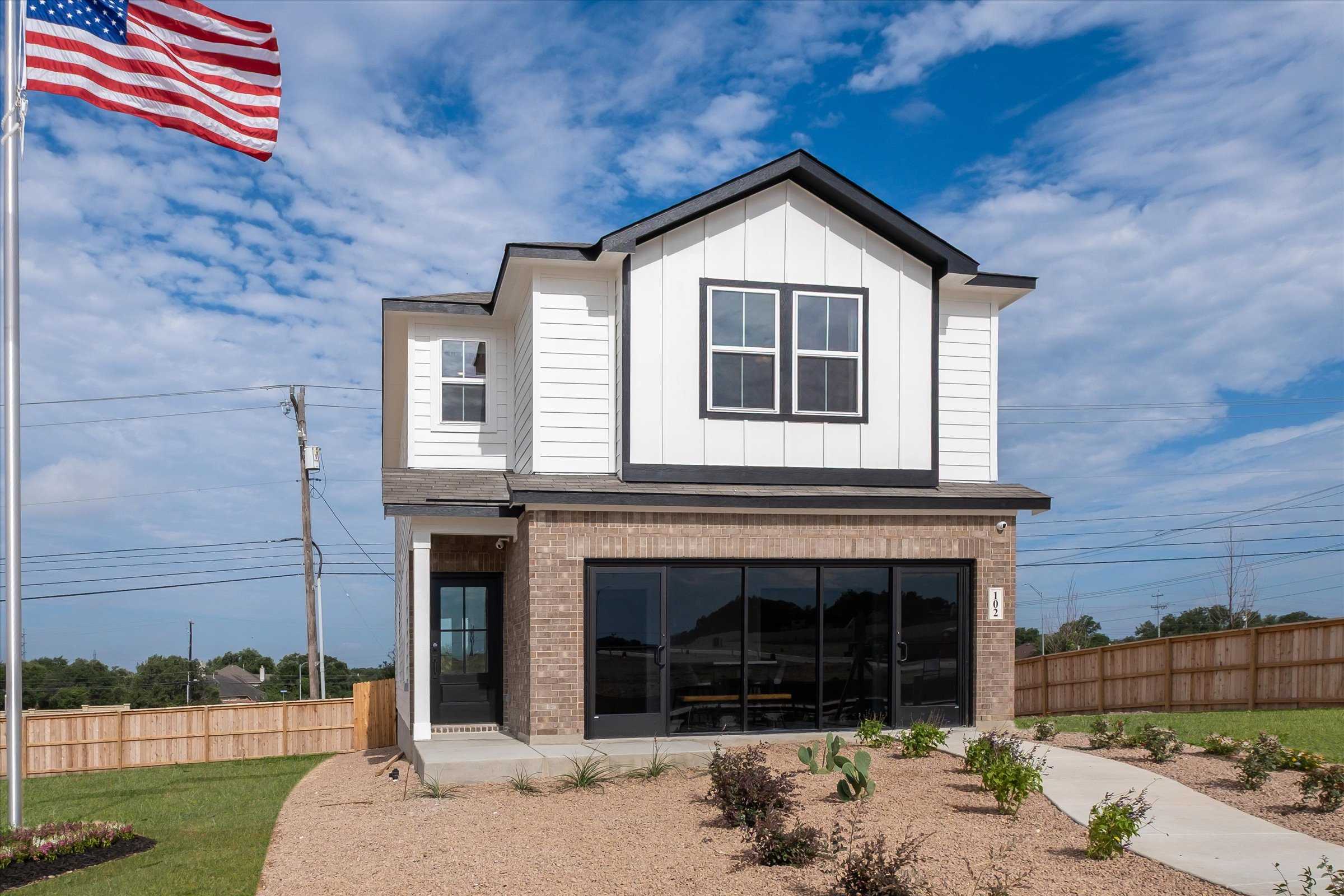 Modern two-story white brick home with American flag, landscaped yard, and wooden fence in Meadows at Oak Creek, San Antonio