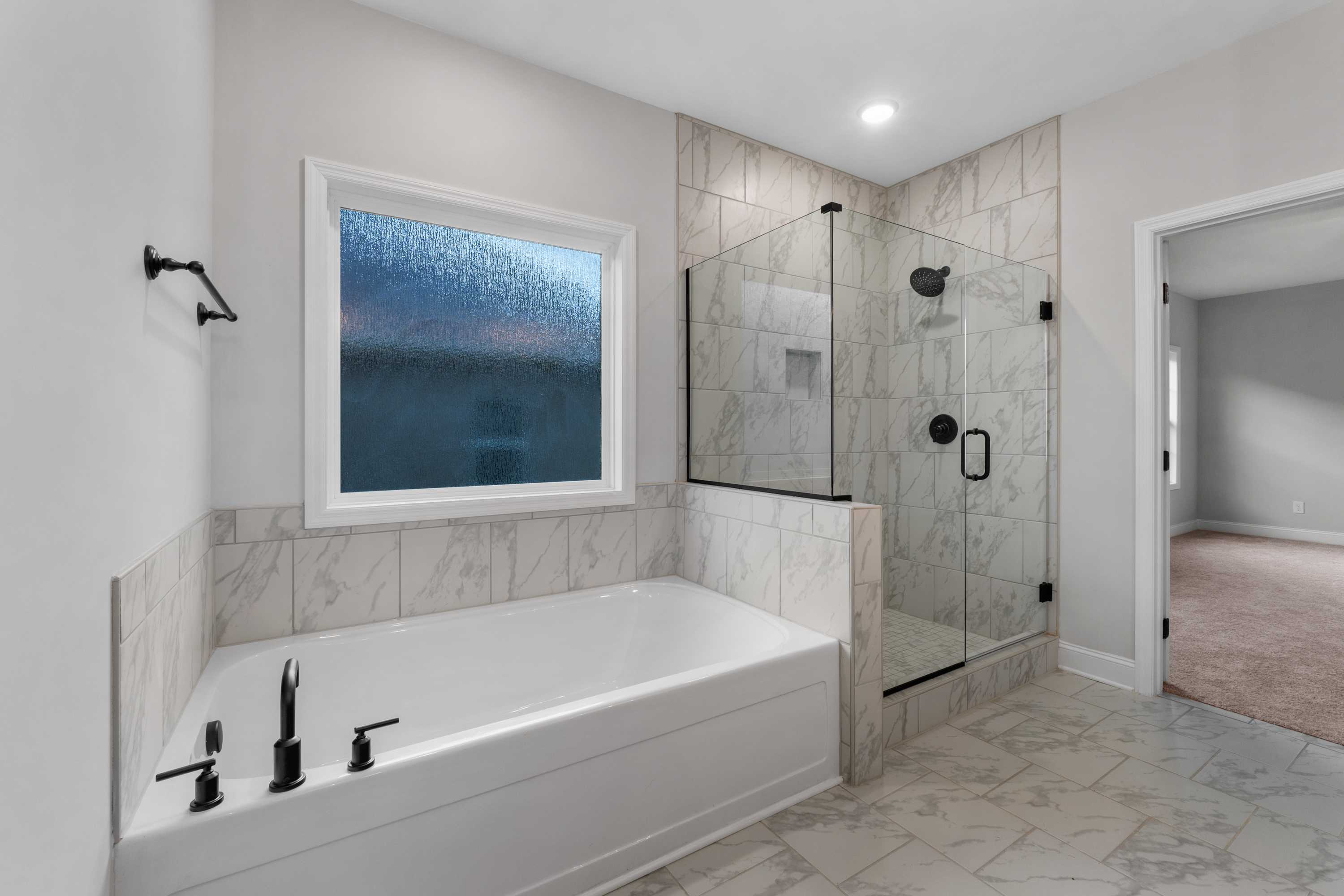 Spacious master bathroom in The Oxford with freestanding tub, glass walk-in shower, and large window