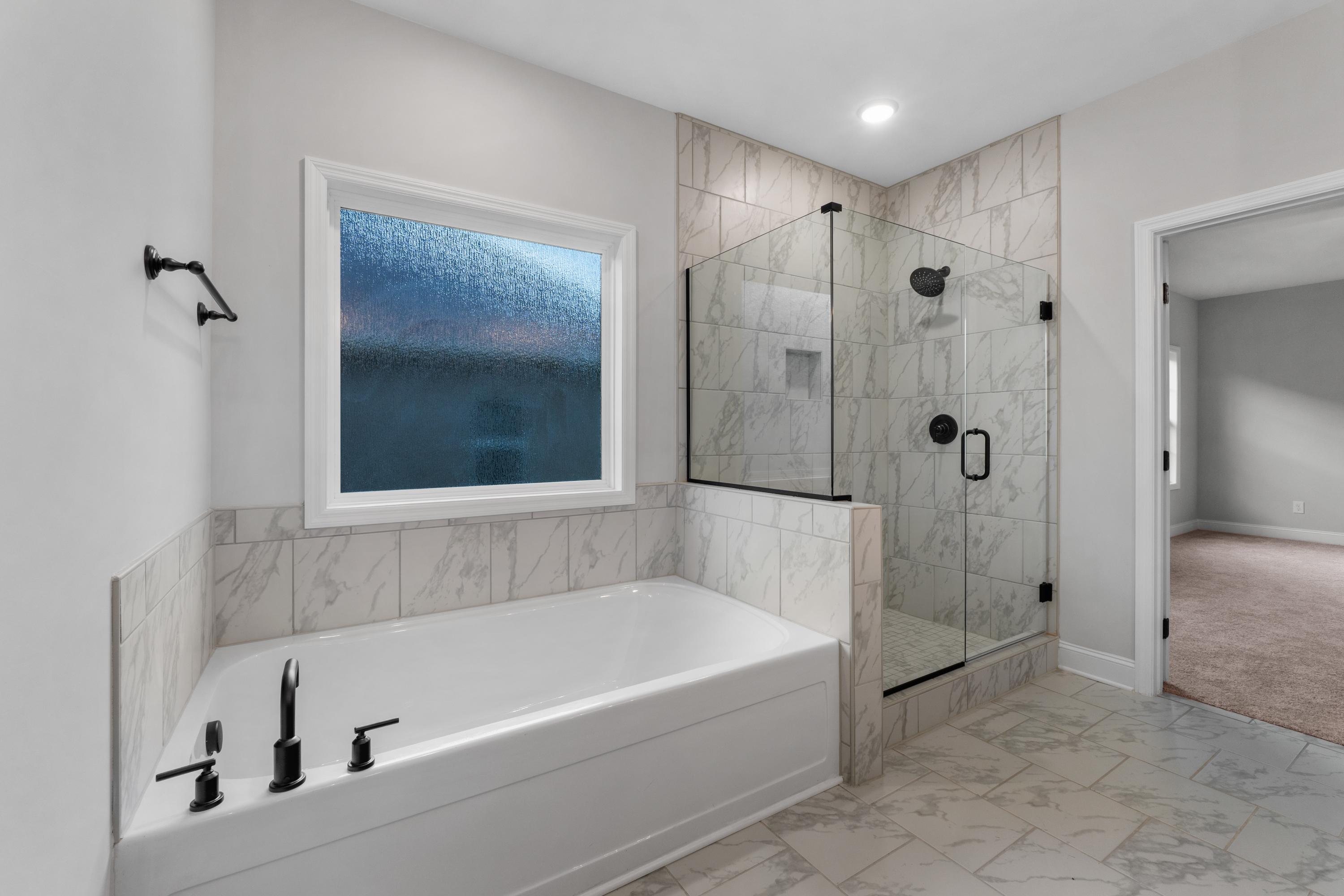 Spacious master bathroom in The Oxford with freestanding tub, glass walk-in shower, and large window