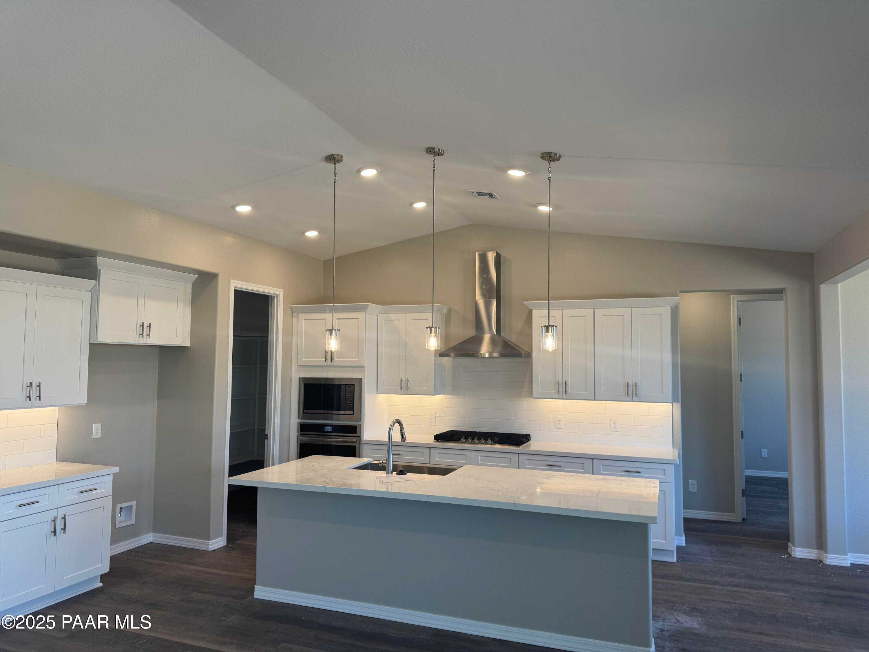 Modern kitchen with white shaker cabinets, quartz island sink, stainless steel range hood in Davidson Homes The Monarch E, Prescott AZ