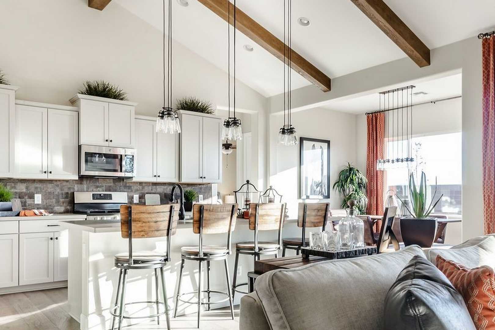 Spacious open-concept kitchen in The Monarch home featuring white cabinetry, large island, wood beam ceiling, and adjacent living area
