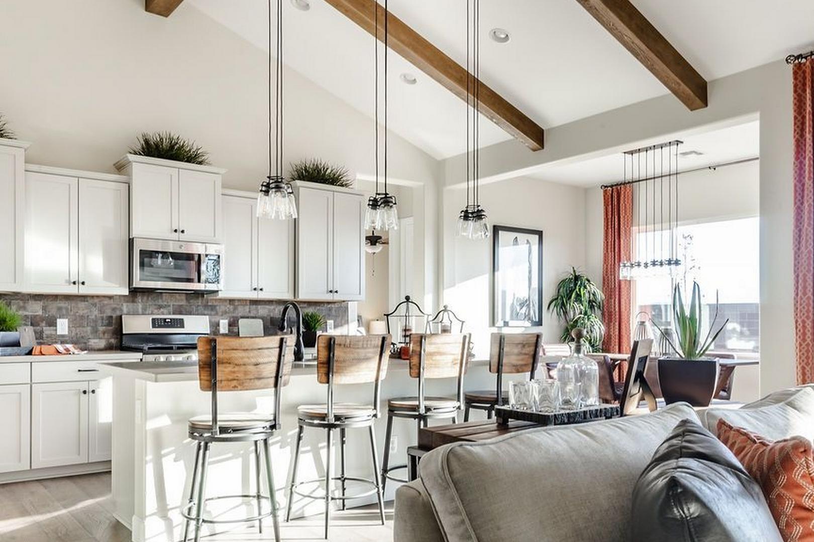 Open-concept kitchen in The Monarch B Evermore Homes, Prescott Valley AZ, featuring white cabinets, large island with bar stools, stainless appliances, wooden beams
