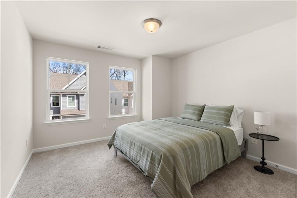 Cozy bedroom with queen bed, green striped duvet, bedside lamp, and large windows overlooking trees in Davidson Homes The Marion B, Kennesaw, Georgia