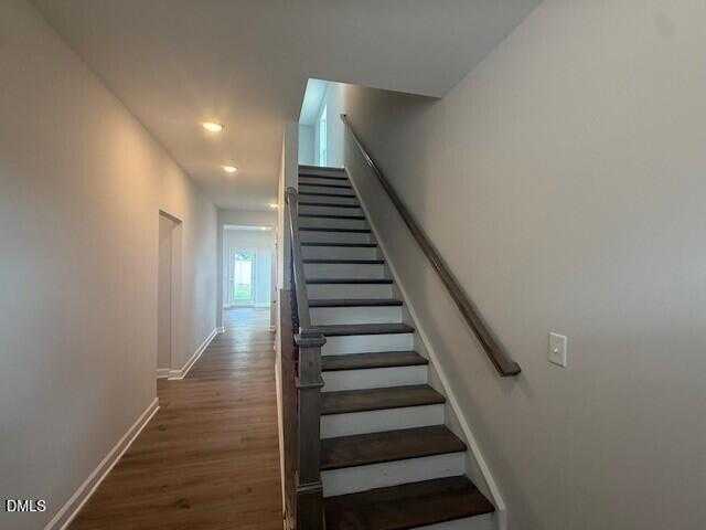Bright hallway with light hardwood floors leading to dark-tread staircase in 4-bedroom The Preston C home, Lillington, NC