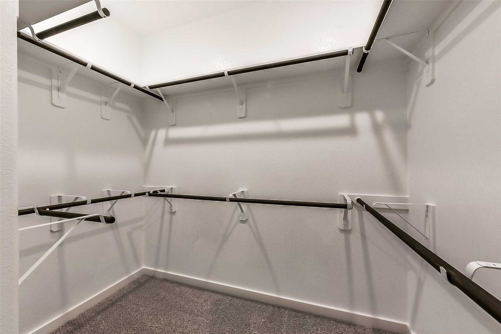 Spacious walk-in closet with black hanging rods, white walls, and carpeted floor in Davidson Homes The Laguna B, Katy, Texas