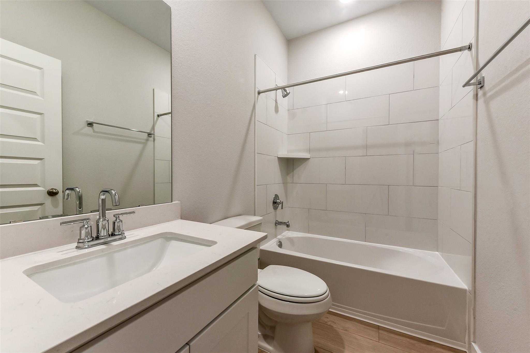 White tiled bathroom with tub-shower combo, modern vanity, toilet in Davidson Homes The Laguna B, Sunterra, Katy, Texas