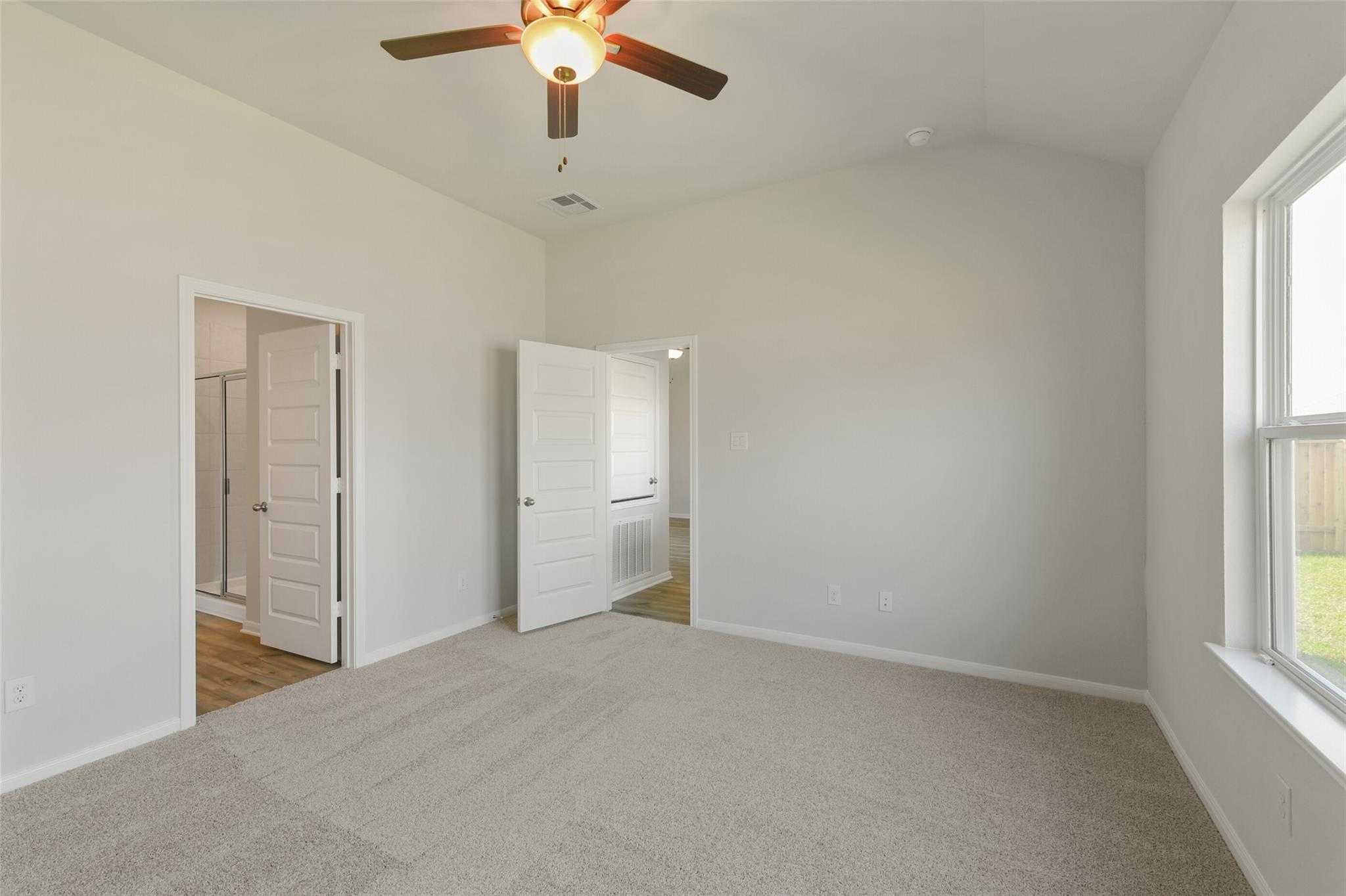 Spacious carpeted master bedroom with ceiling fan, en-suite bath door, and window to backyard in Davidson Homes The Laguna B, Dayton, Texas