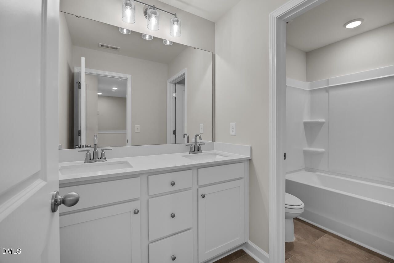 Spacious bathroom featuring double white vanity, large mirror, bathtub, and shower in Davidson Homes The Avery, Knightdale, NC