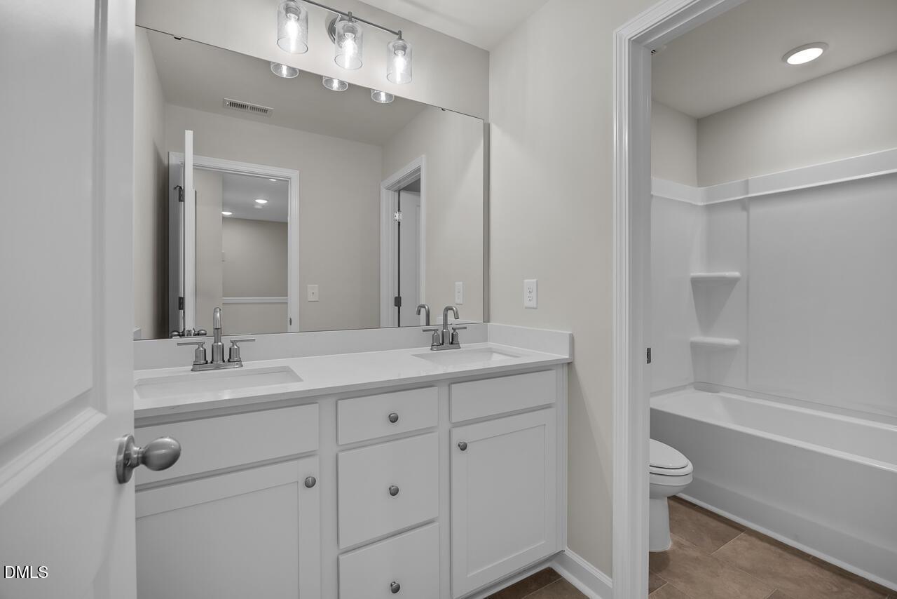 Spacious bathroom featuring double white vanity, large mirror, bathtub, and shower in Davidson Homes The Avery, Knightdale, NC