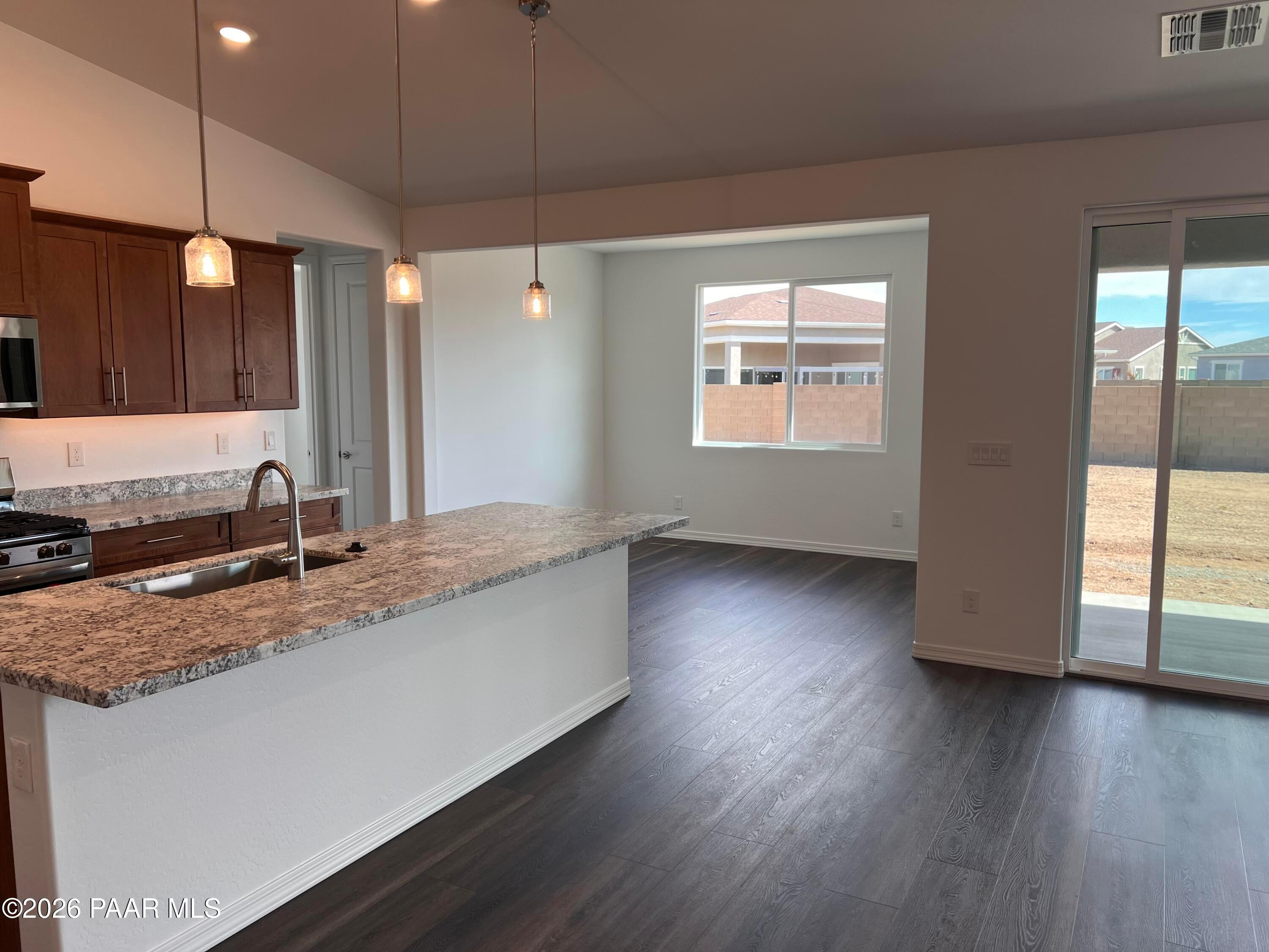 Modern kitchen with granite island sink, stainless appliances, dark cabinets, and open living space in Davidson Homes The Monarch A, Prescott AZ