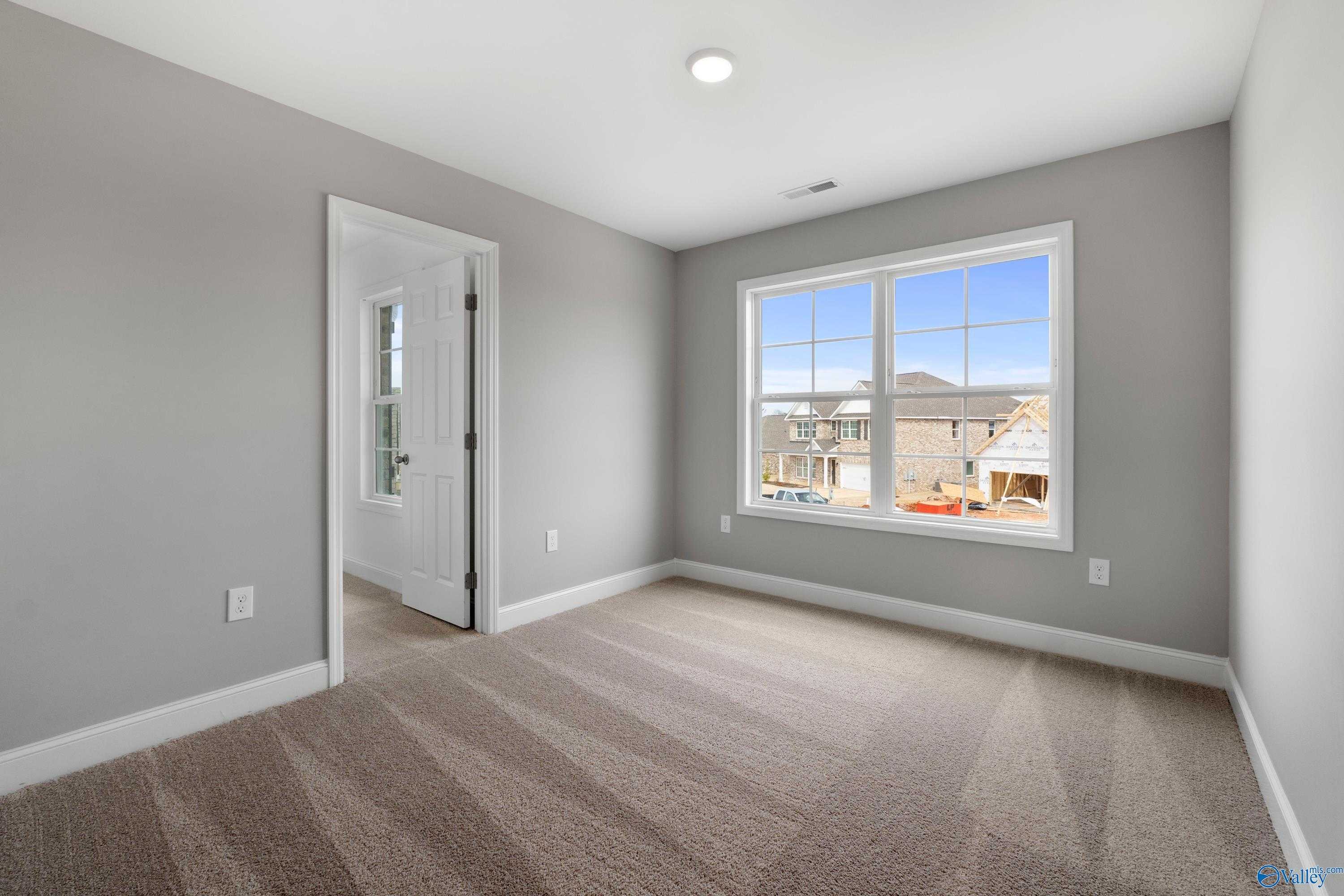 Bright secondary bedroom with gray walls, carpeted floor, and window view of new homes in Walker's Hill, Meridianville, The Aiken by Davidson Homes