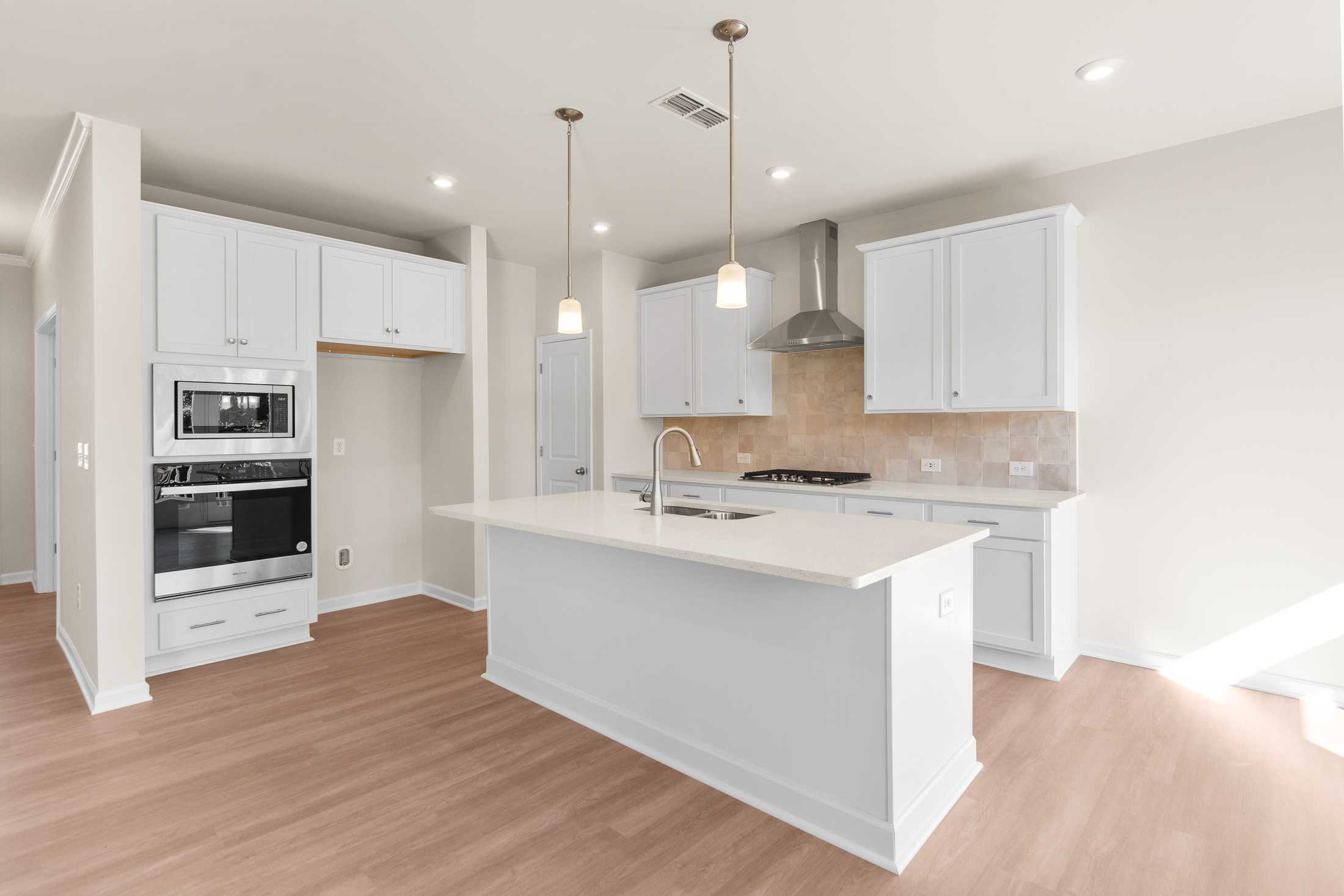Modern white kitchen in The Willow B home featuring large island, stainless steel appliances, and pendant lights