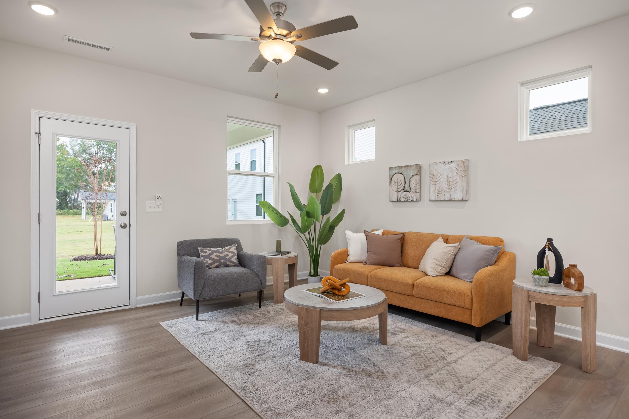 Modern living room at Gregory Village in Lillington, NC, featuring an orange sofa, grey armchair, and wood-toned decor.
