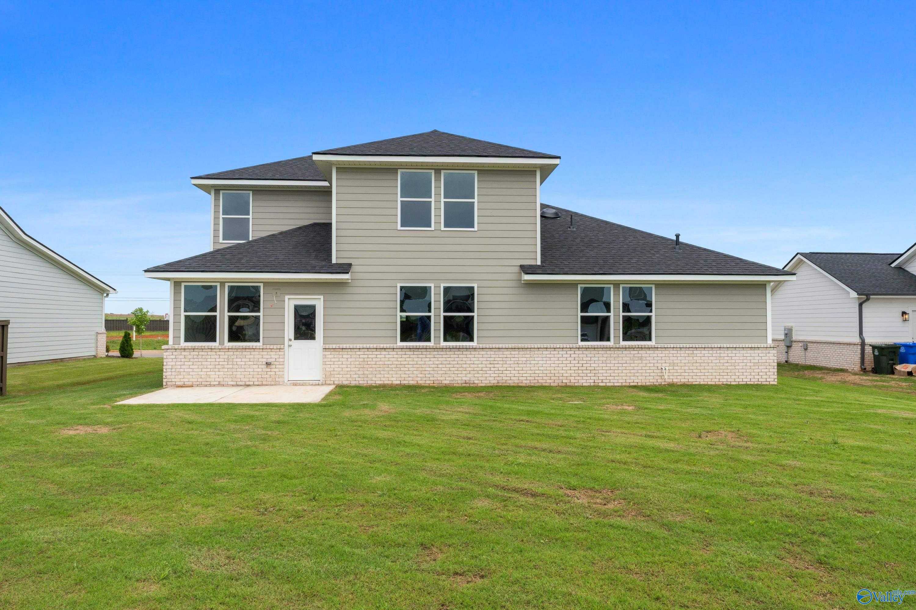 Two-story Dorado home rear with beige siding, windows, back door, concrete patio, and lush green yard in Anderson Farm, Athens, Alabama
