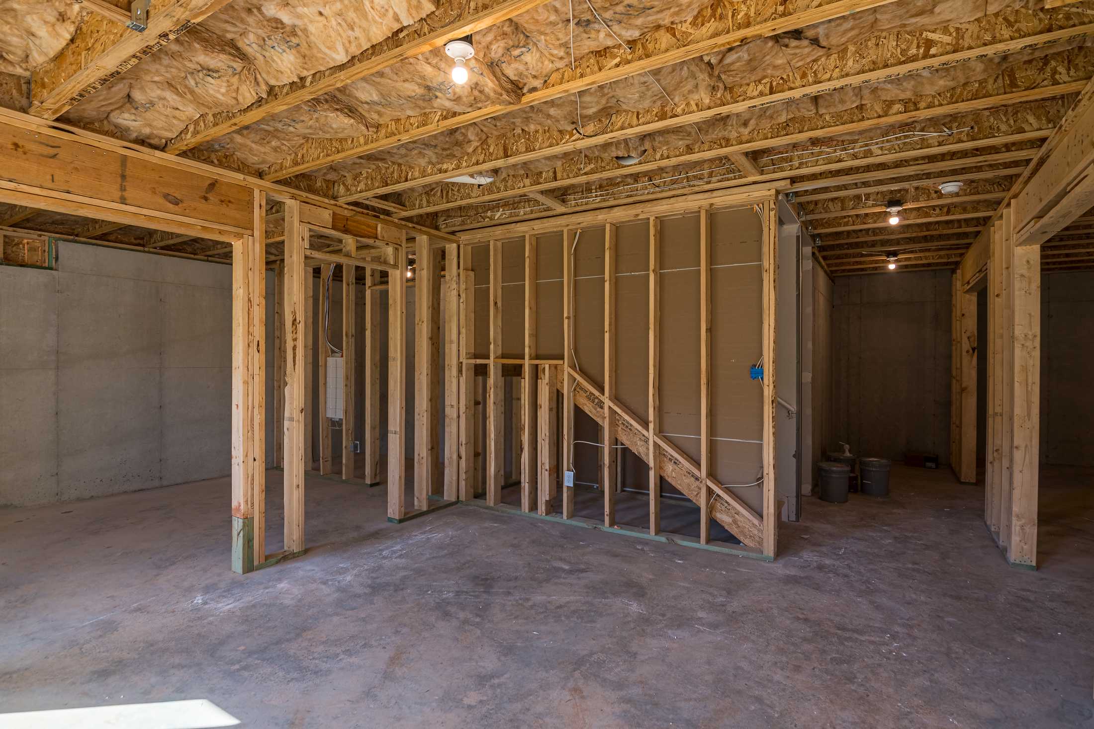 Framing stage of The Willow B home in Wehunt Meadows, showcasing wooden studs, ceiling insulation, staircase, and 2-car garage bays