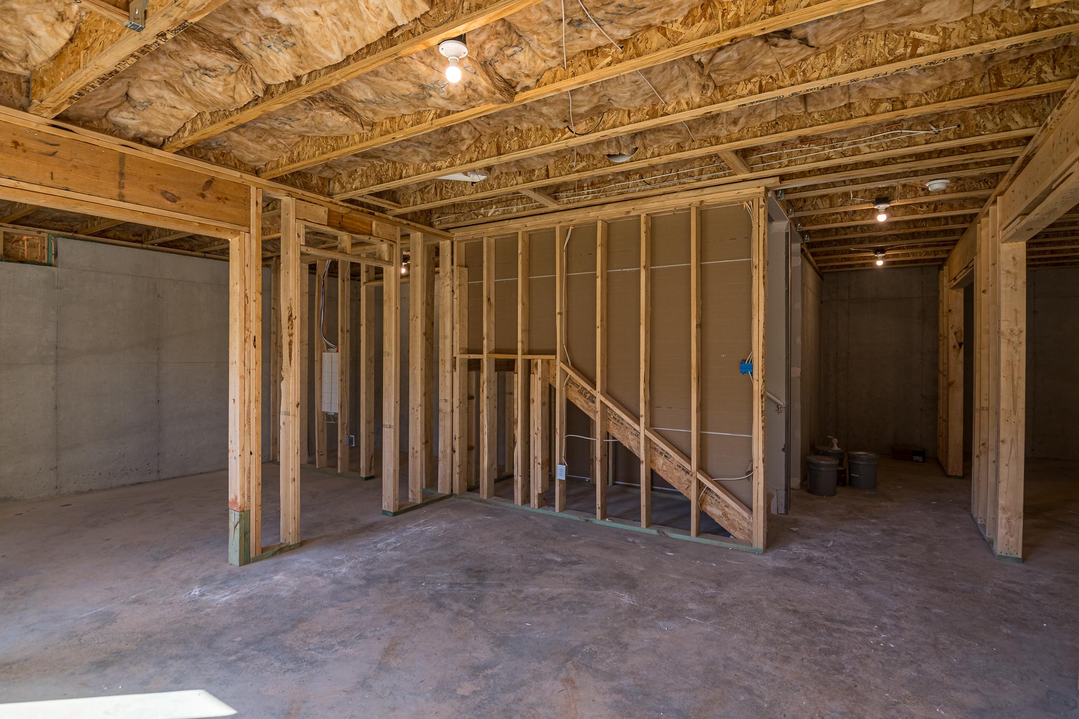 Framing stage of The Willow B home in Wehunt Meadows, showcasing wooden studs, ceiling insulation, staircase, and 2-car garage bays