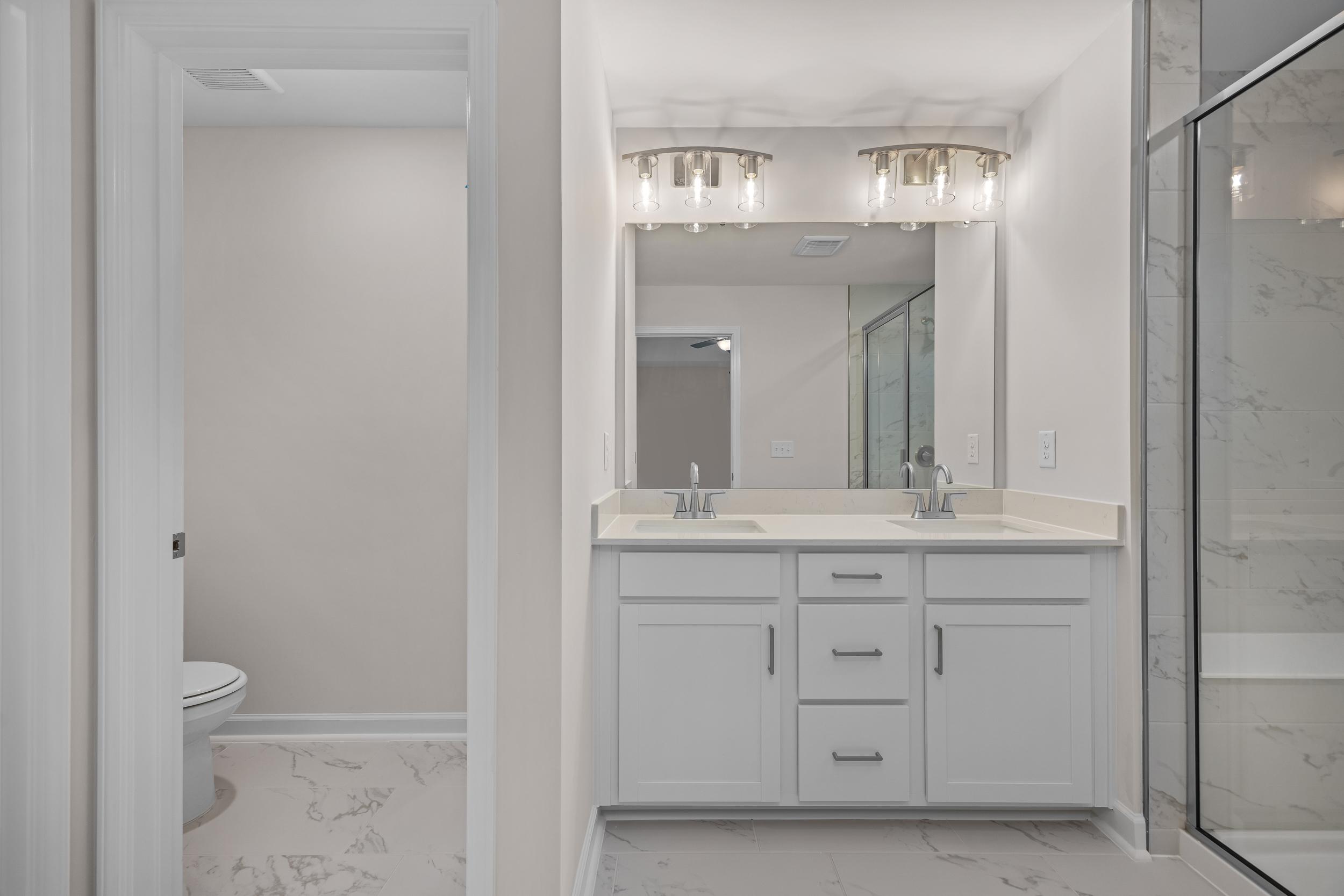 Spacious primary bathroom with double vanity, frameless glass shower, white cabinets at Forestville Yard Townhomes in Knightdale NC