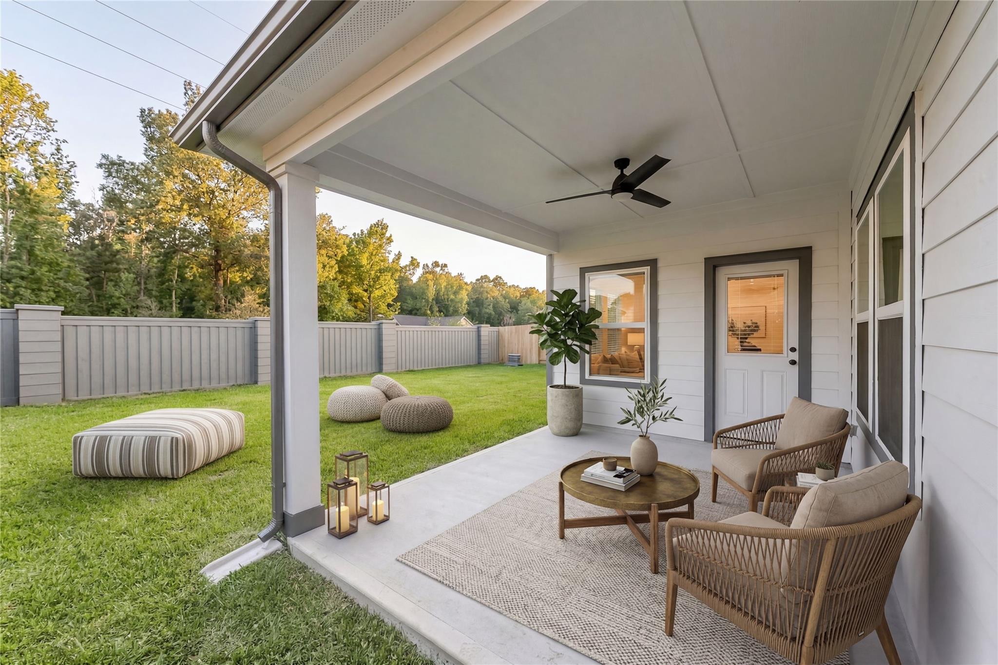 Covered back patio with rattan furniture, potted plants, lanterns, and lush lawn in Davidson Homes The Everett C, Sundance Cove, Crosby, Texas