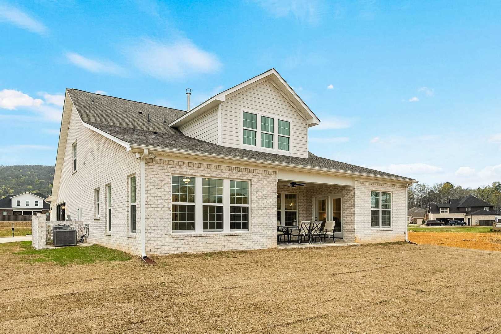 Two-story The Oxford home elevation by Evermore Homes featuring white siding, brick accents, covered porch with seating, and rural Alabama landscape