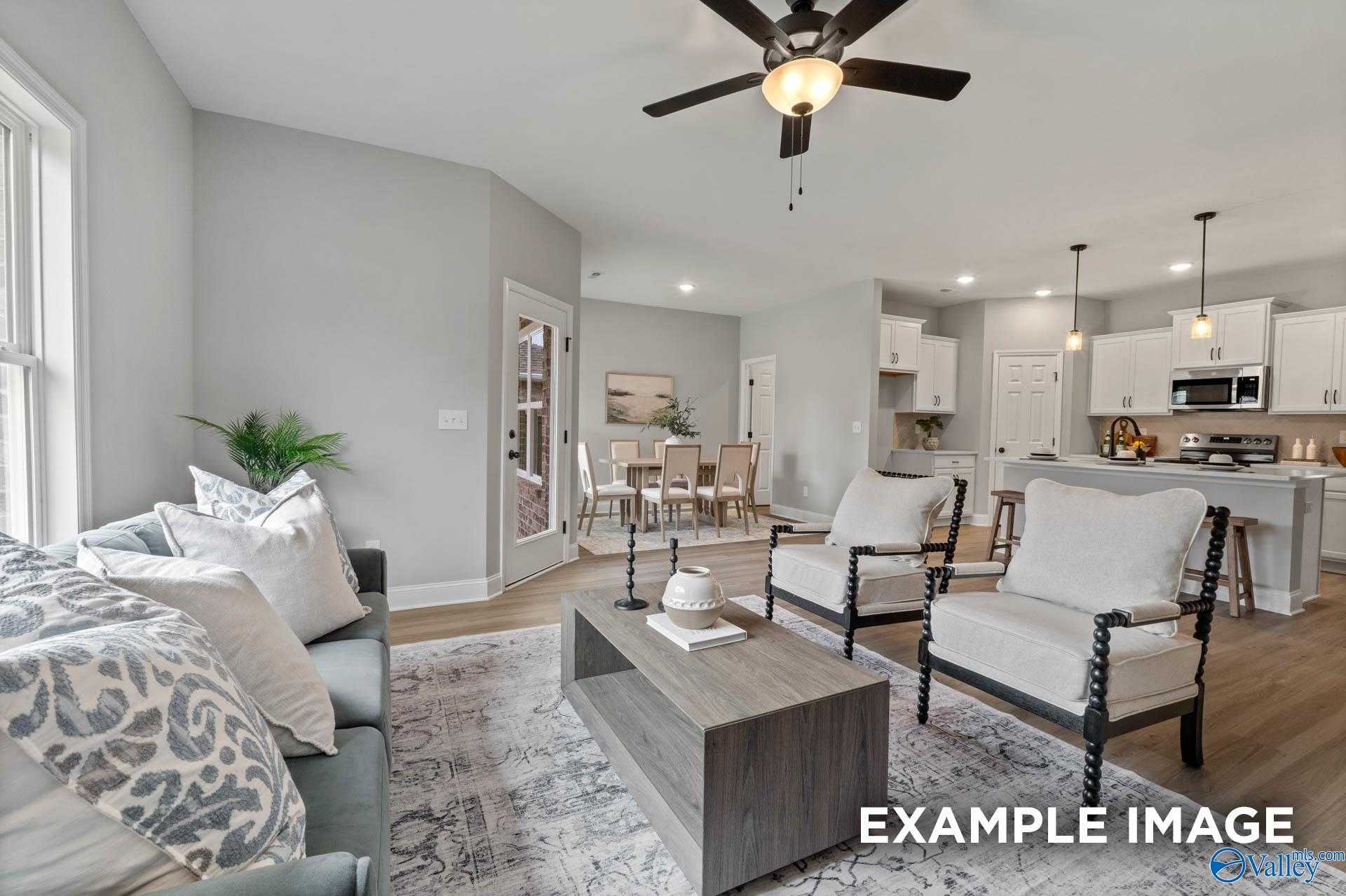 Open-concept living and dining area with gray sectional sofa, wooden coffee table, white armchairs, and adjacent kitchen in Davidson Homes The Daphne C, Owens Cross Roads