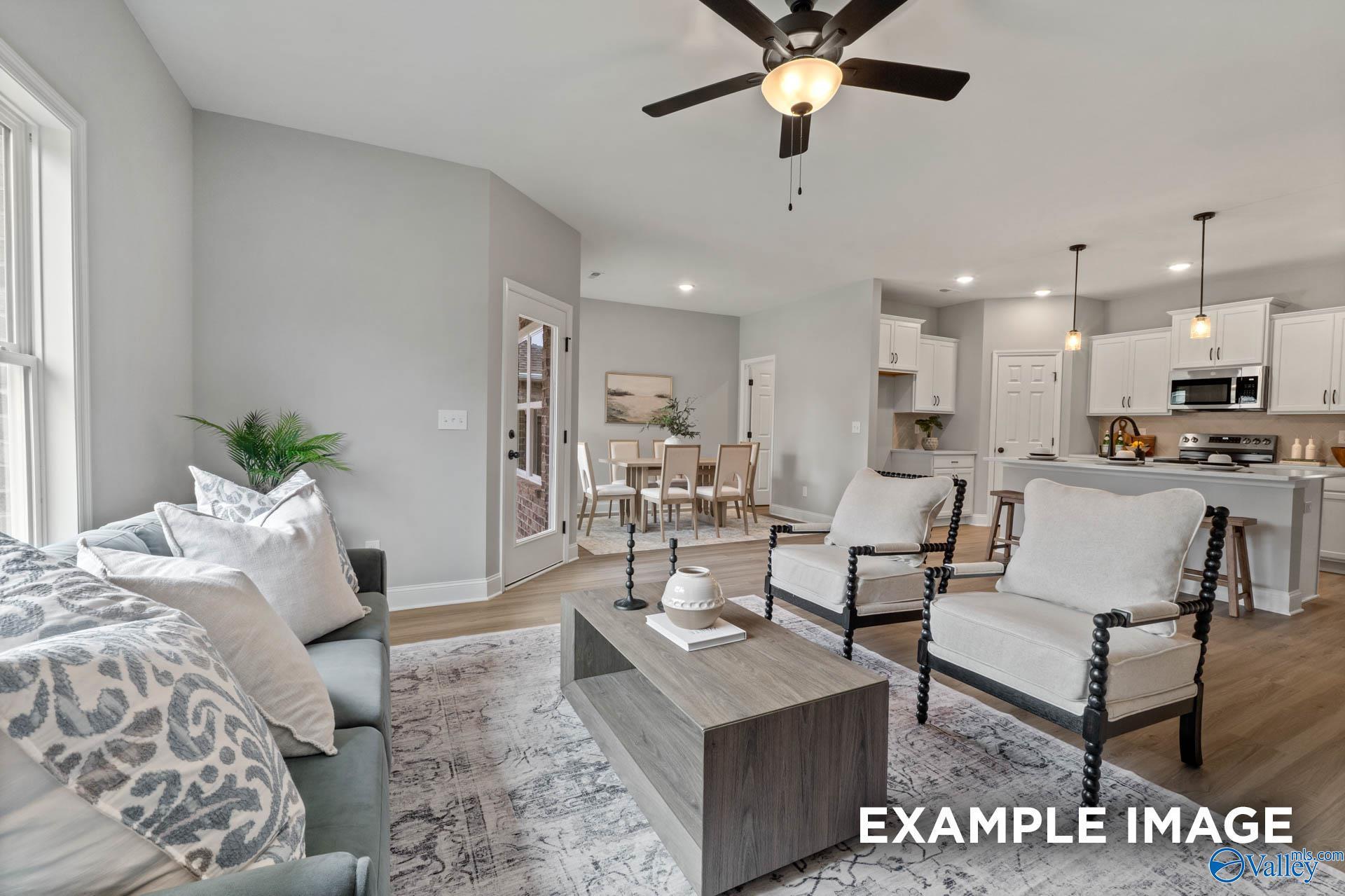 Open-concept living and dining area with gray sectional sofa, wooden coffee table, white armchairs, and adjacent kitchen in Davidson Homes The Daphne C, Owens Cross Roads