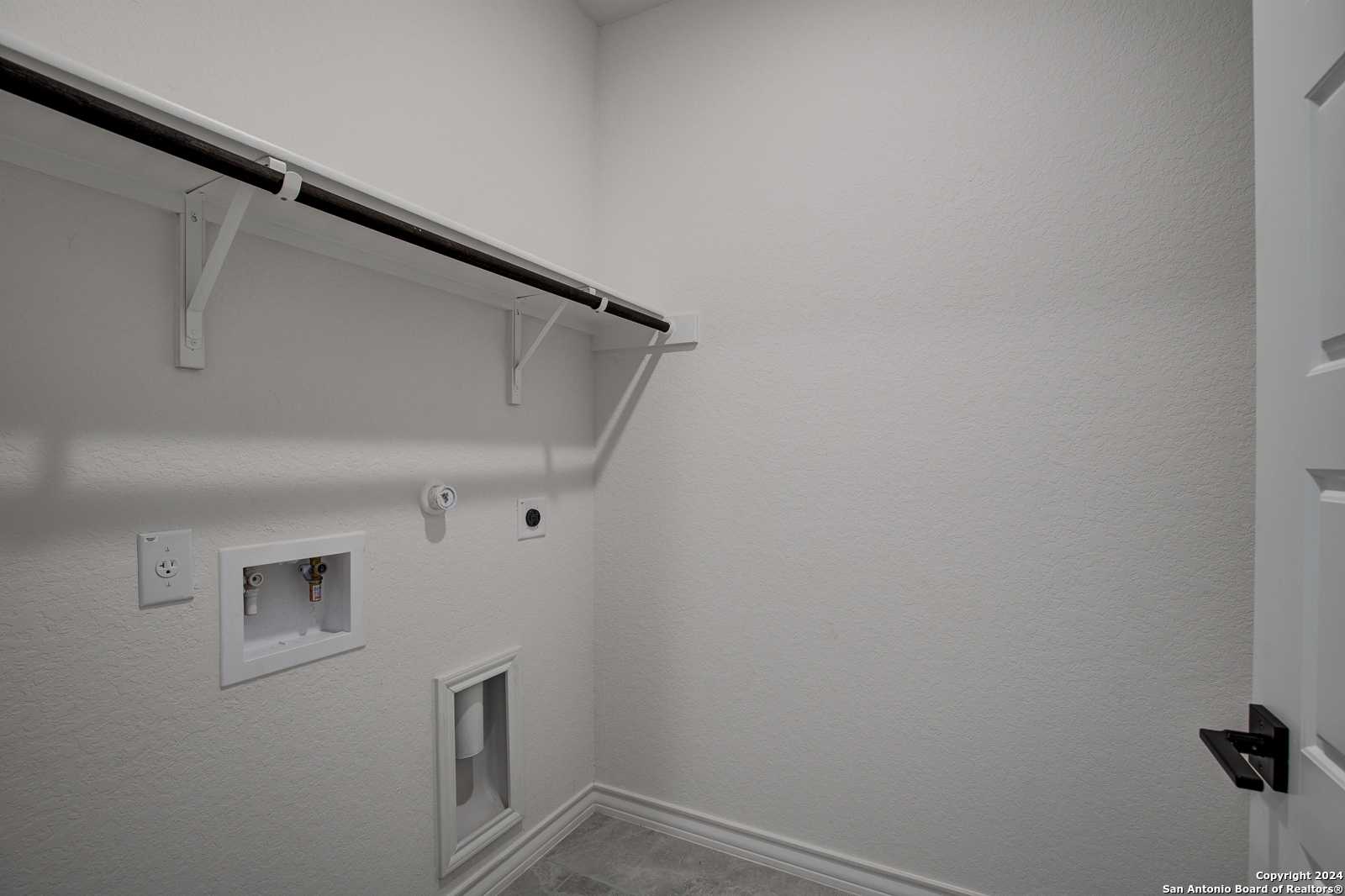 Modern laundry room with hanging rod, washer/dryer hookups in Davidson Homes The Garner B, Castroville, Texas