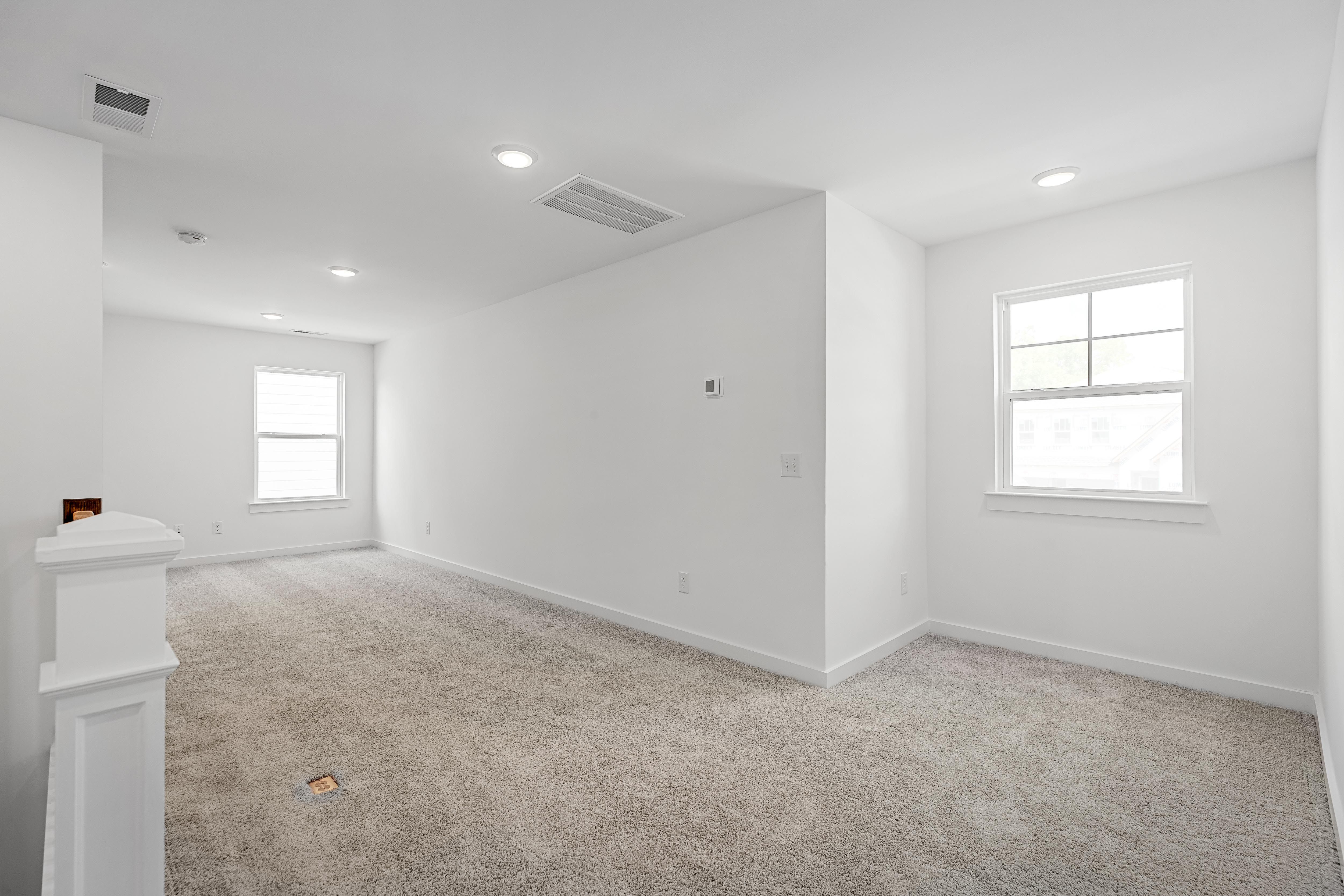 Bright, open multipurpose loft area in The Cedar by Davidson Homes featuring plush carpeting and recessed lighting.
