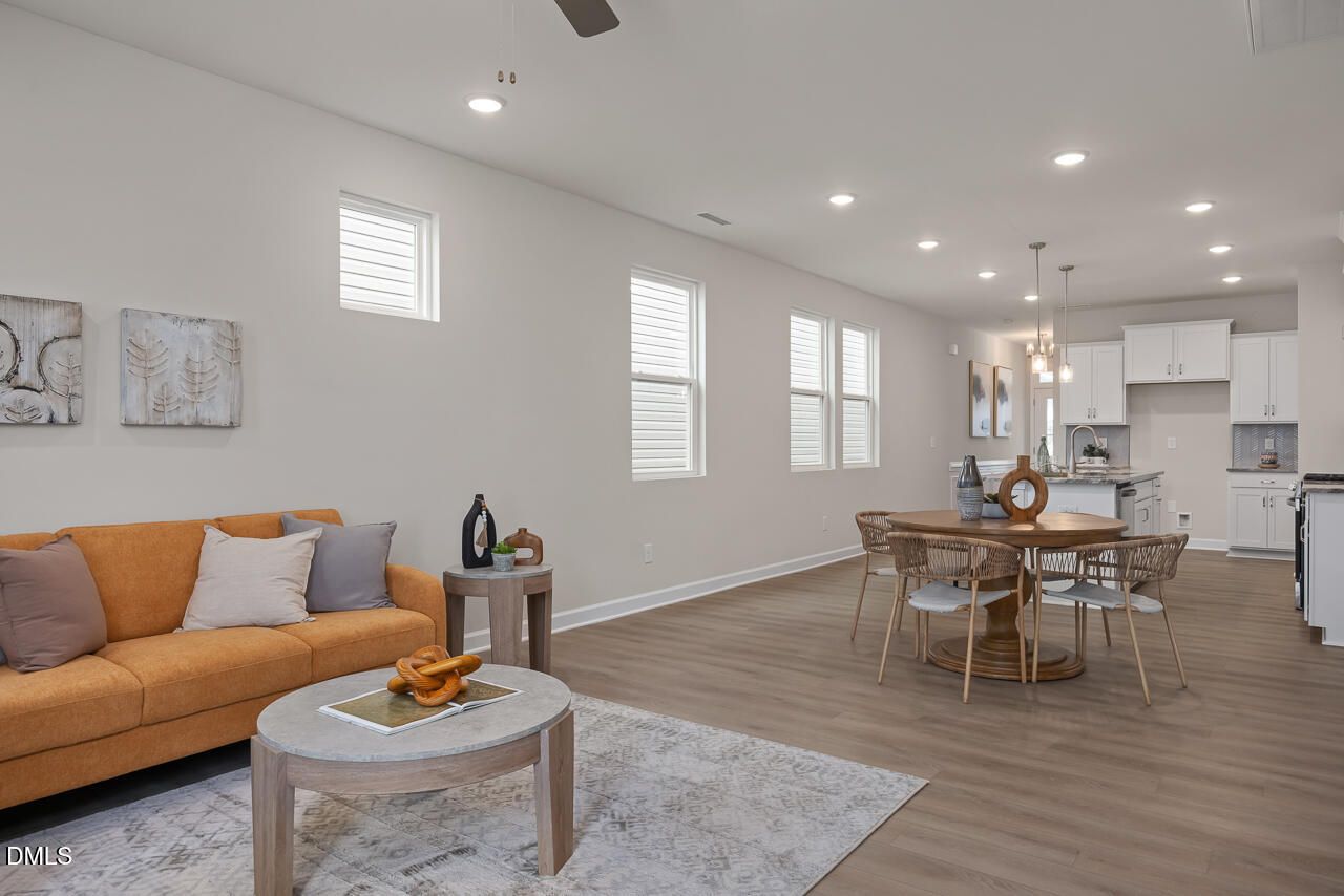 Open-concept living and dining area with orange sofa, round pedestal table, white kitchen cabinets, hardwood floors in Davidson Homes The Carter C, Lillington, NC