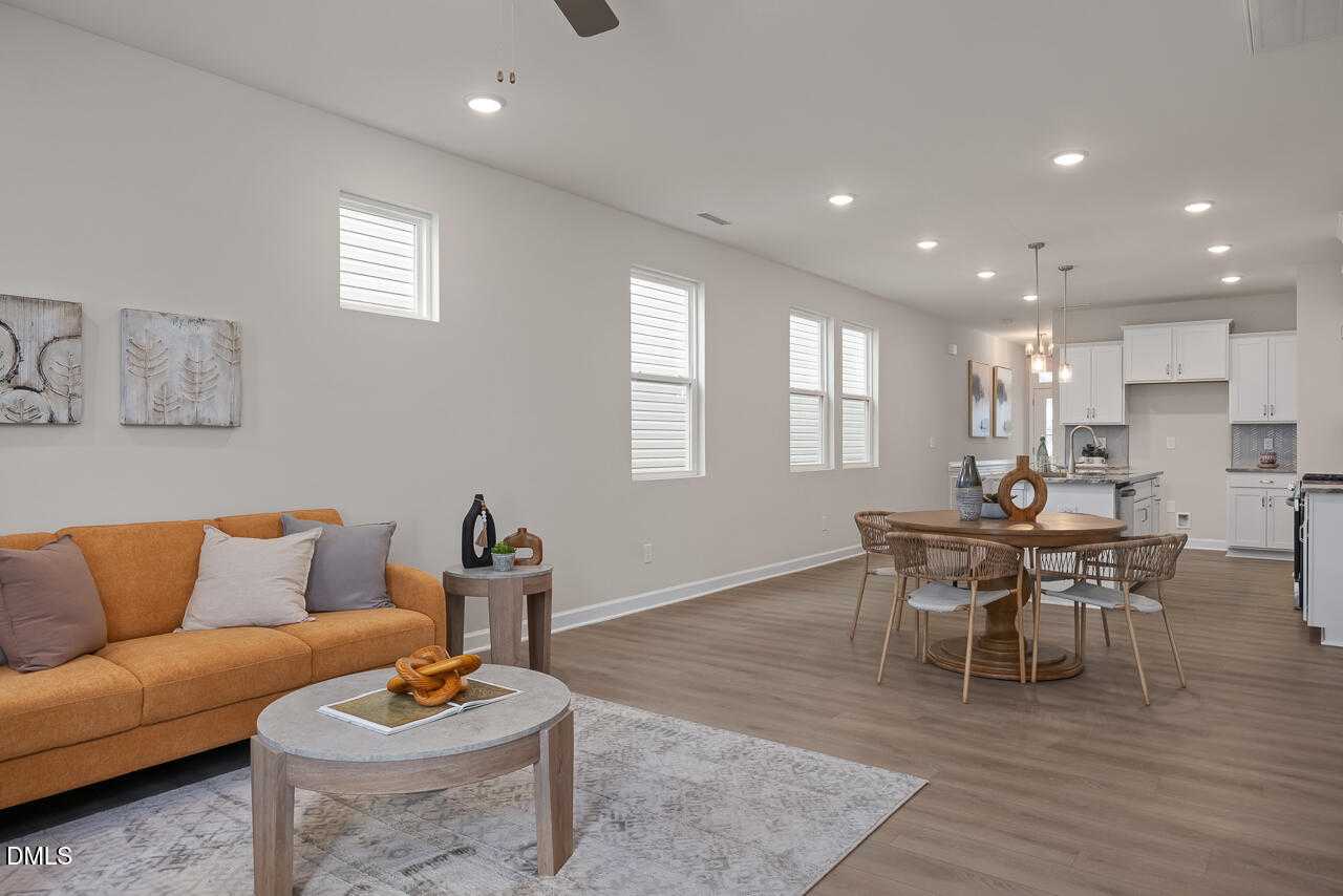 Open-concept living and dining area with orange sofa, round wood table, white kitchen cabinets in Davidson Homes The Carter C, Lillington, NC