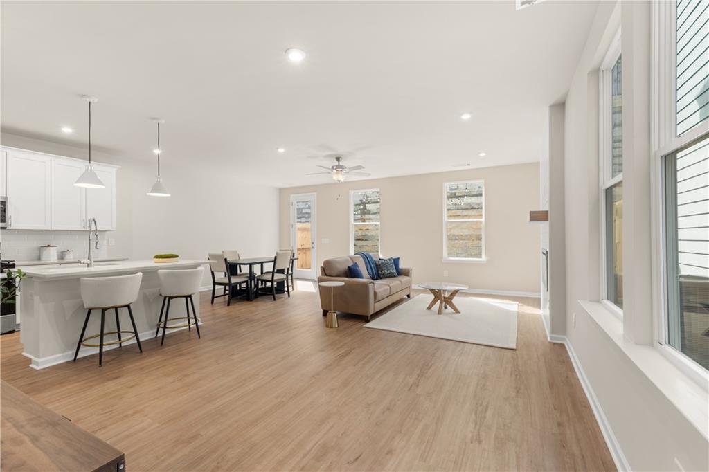 Open-concept kitchen and living room with white island, hardwood floors, beige sofa, and dining table in Davidson Homes The Marion B, Kennesaw, GA