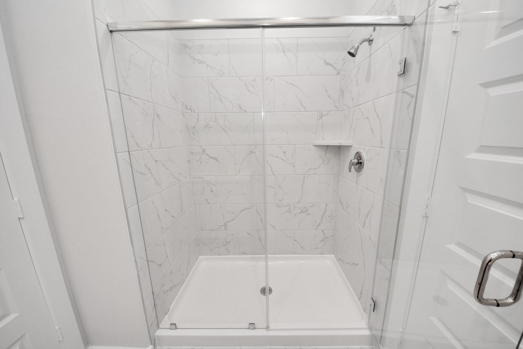Walk-in shower with white marble-look tile and glass sliding doors in a Sabine E floor plan home in Magnolia, Texas.