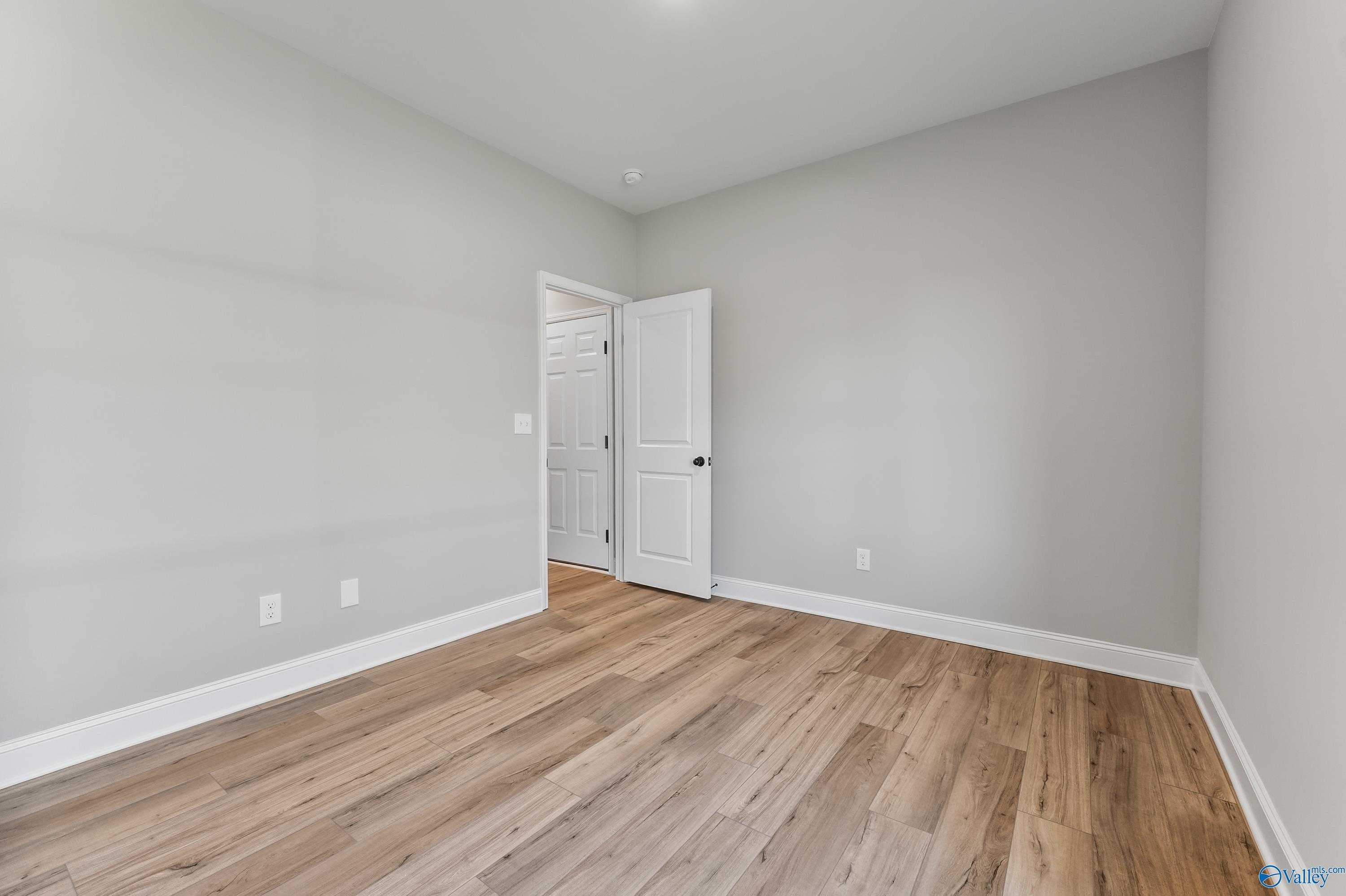 Bright secondary bedroom with light gray walls, white door, and hardwood floors in Davidson Homes The Daphne C, Hazel Green, Alabama