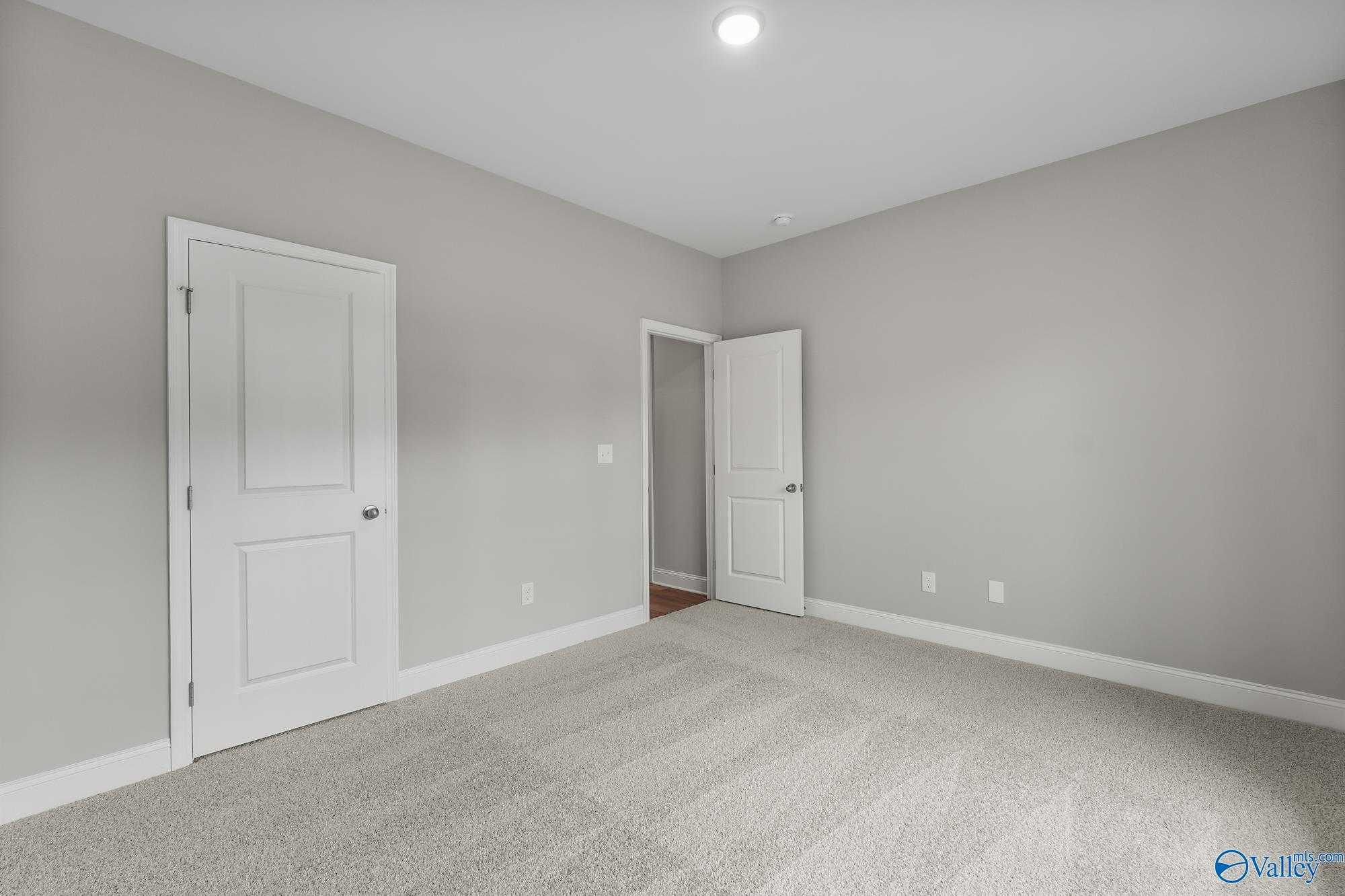 Spacious empty bedroom with light gray walls, white doors, and carpet flooring in Davidson Homes The Daphne D, Athens AL