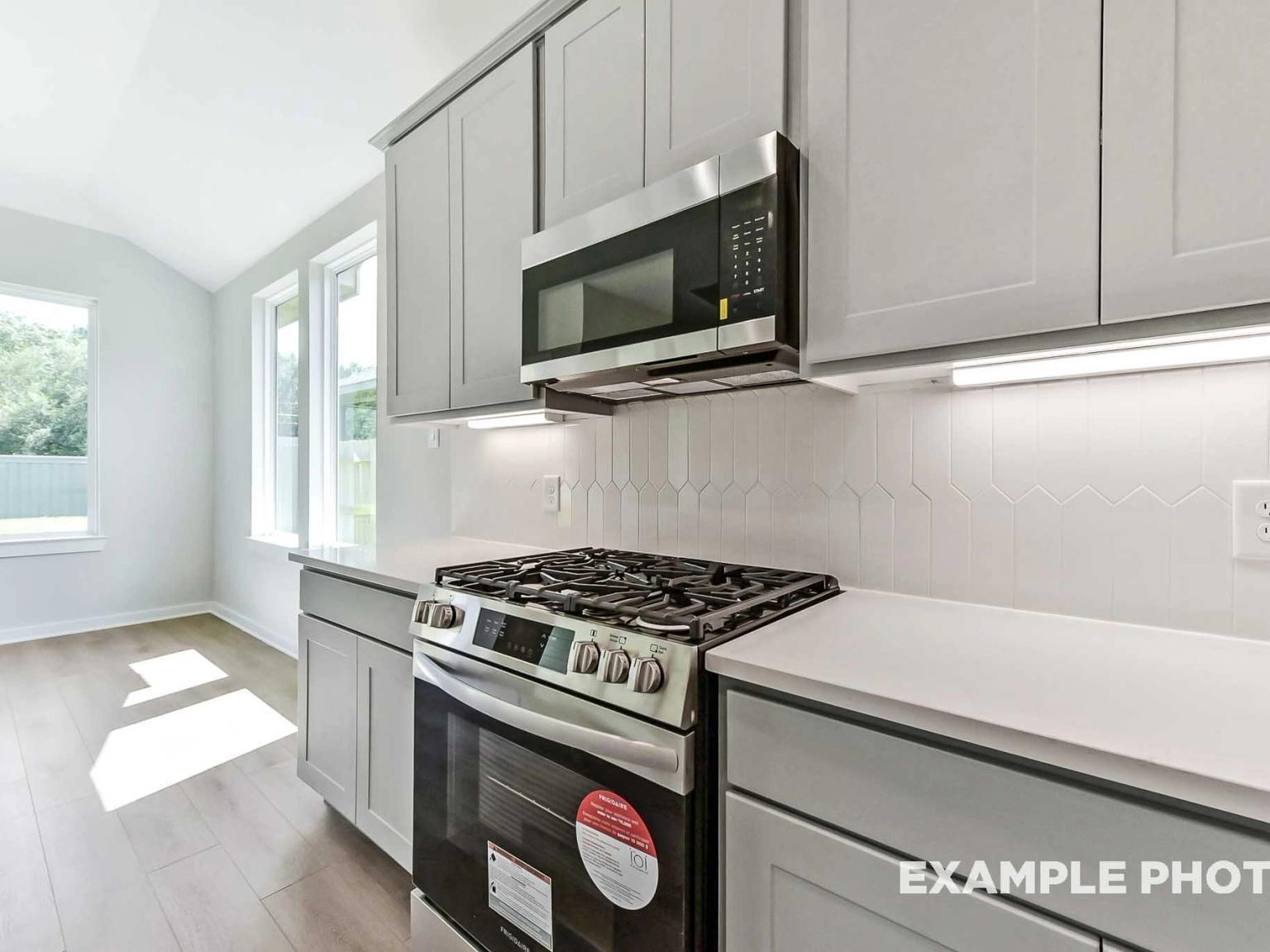 Modern kitchen with gray cabinets, stainless steel gas range, and herringbone tile backsplash in Sundance Cove, Crosby.