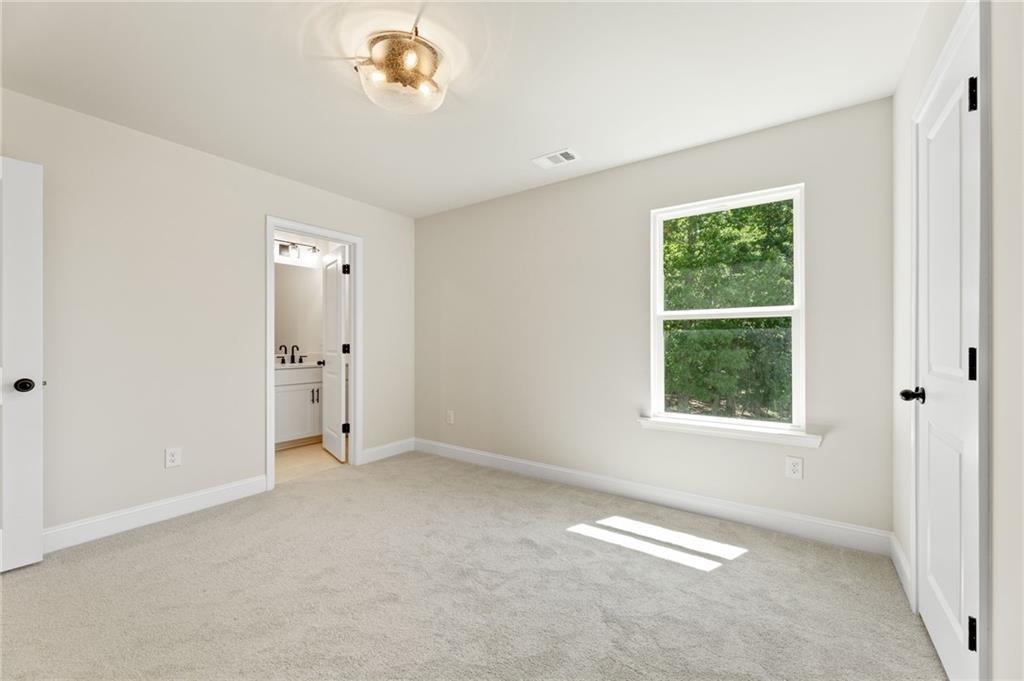Bright secondary bedroom with beige walls, large window to greenery, and bathroom door in Davidson Homes The Hickory E, Buford, GA