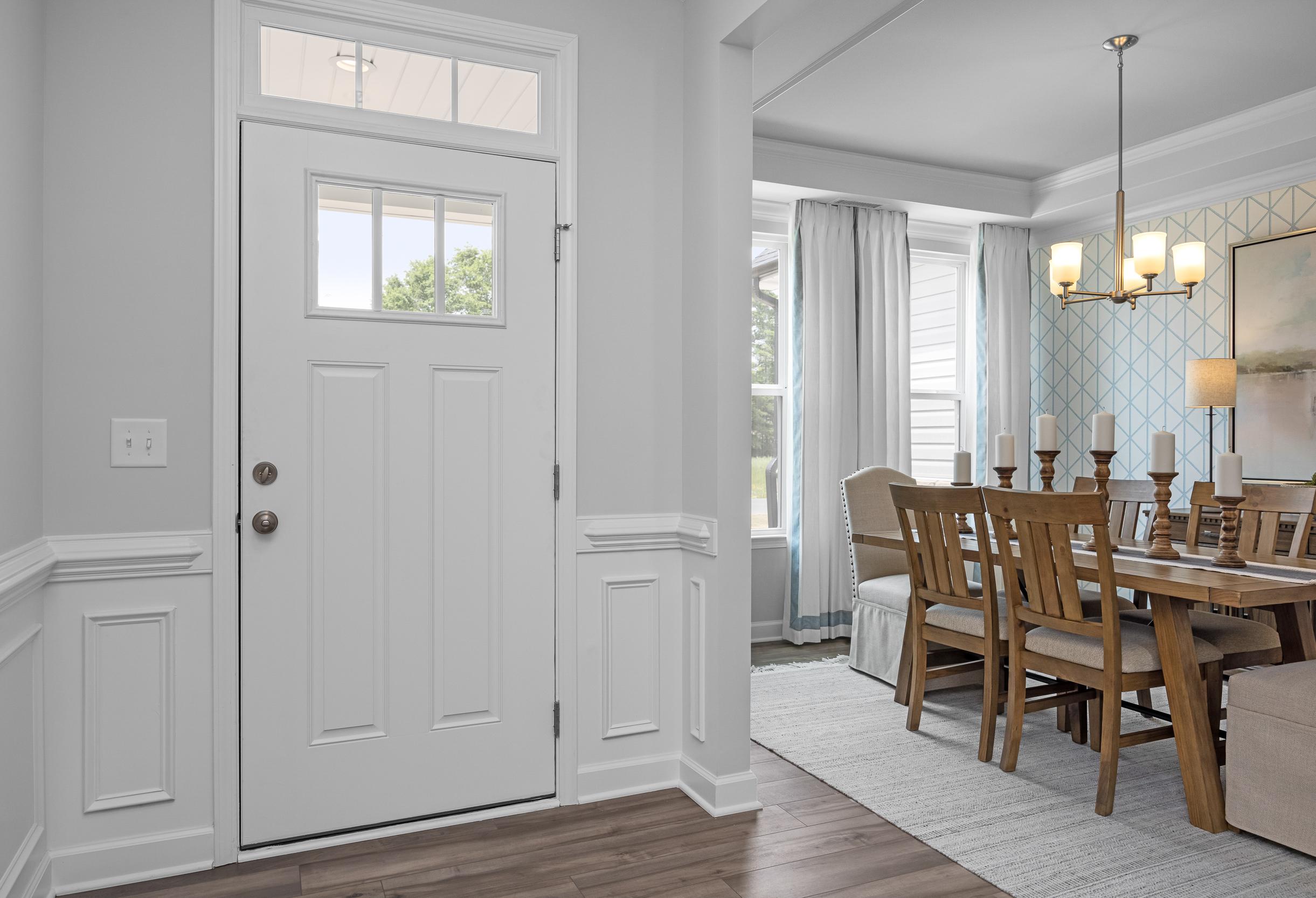 Open entryway and dining area in The Magnolia A home, white paneled door, chandelier, wooden table, curtains, Holly Springs NC