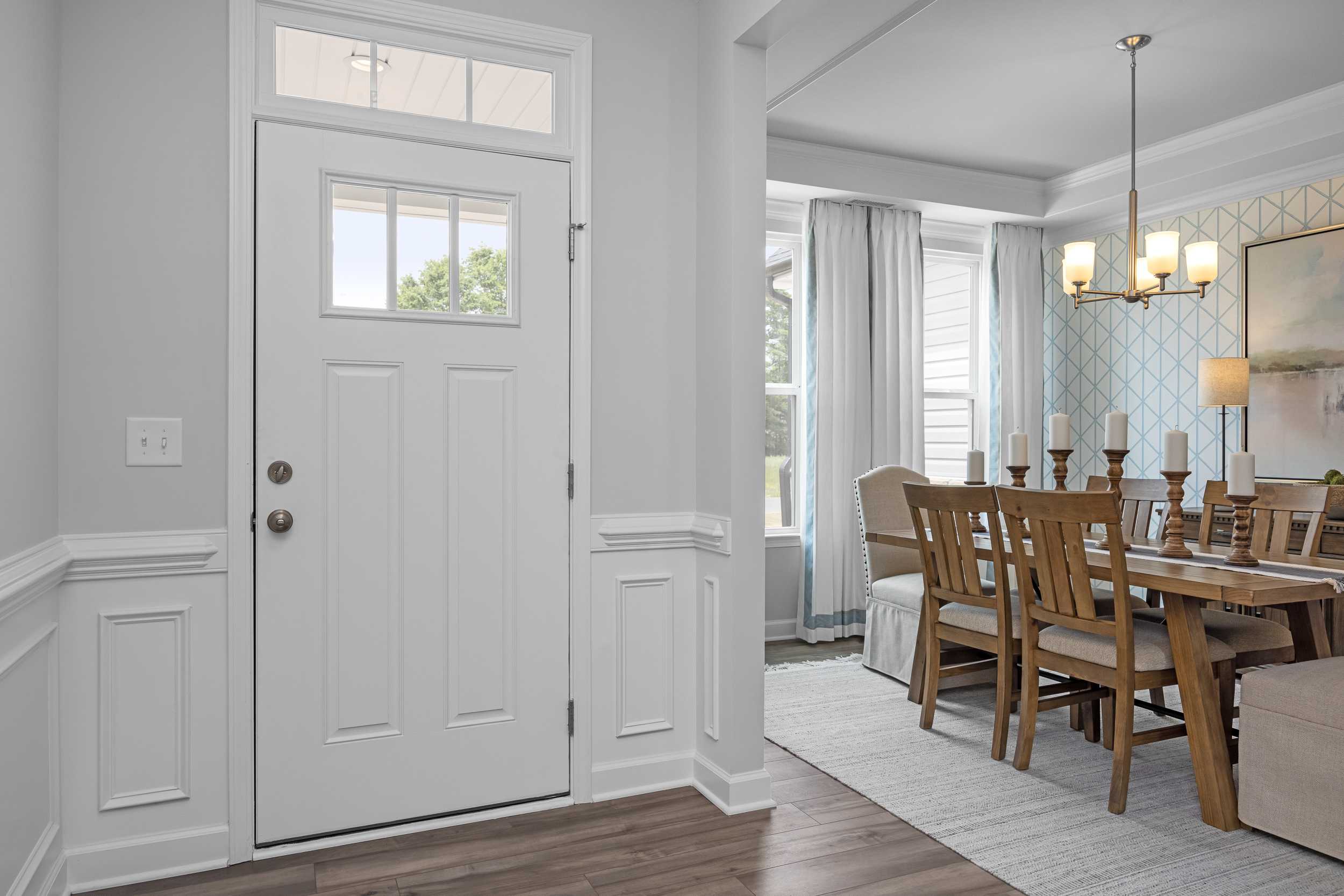 Spacious entryway opening to dining area in The Magnolia A, featuring white paneled door, wooden table, and chandelier