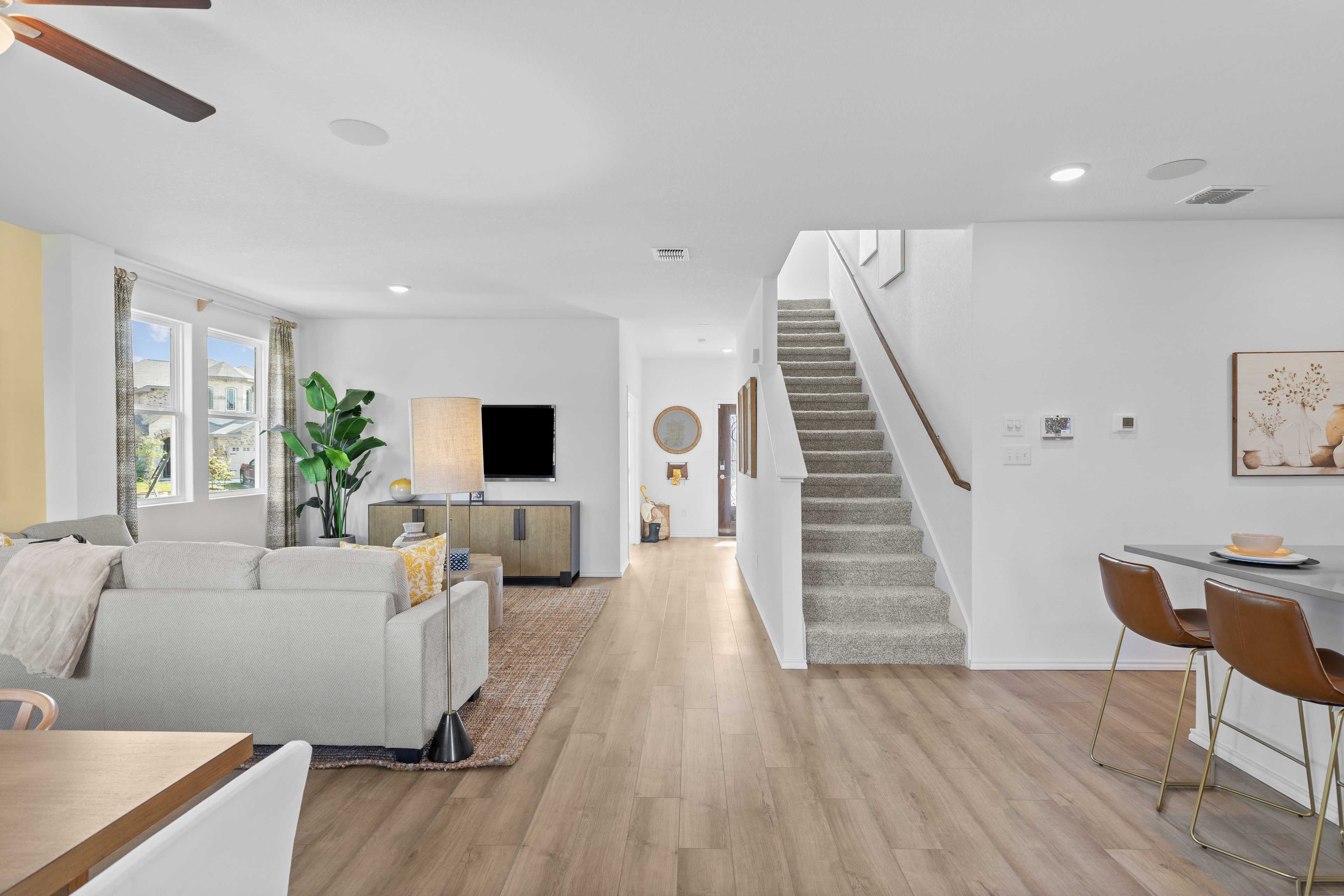 Spacious open-concept living room at Horizon Pointe in Converse TX with beige sofa, hardwood floors, TV, plants, and carpeted staircase
