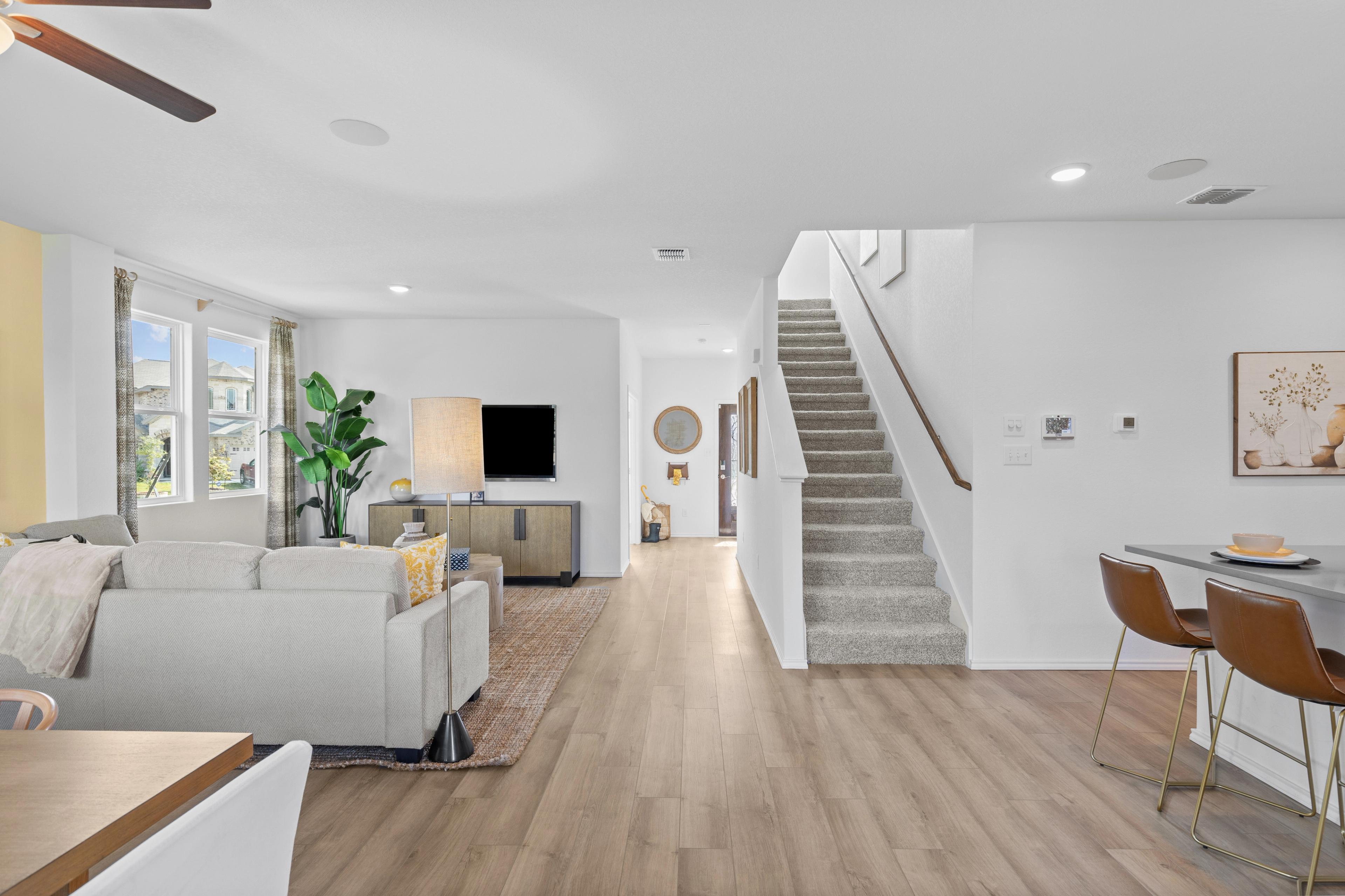 Spacious open-concept living room at Horizon Pointe in Converse TX with beige sofa, hardwood floors, TV, plants, and carpeted staircase