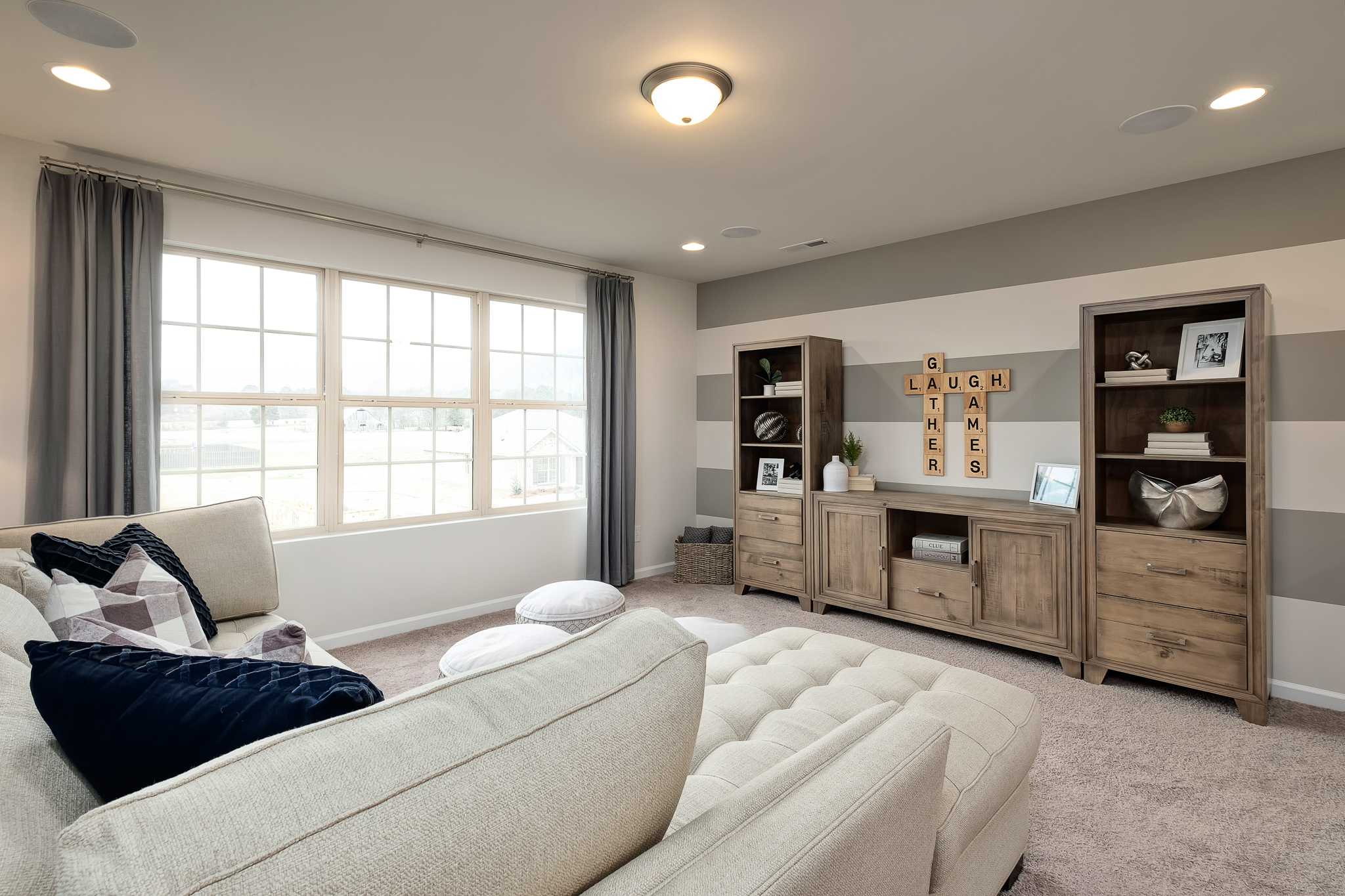 Cozy beige sectional sofa in modern living room at The Reserve at Overton, Hampton Cove AL with wooden media console, bookshelves, and large windows