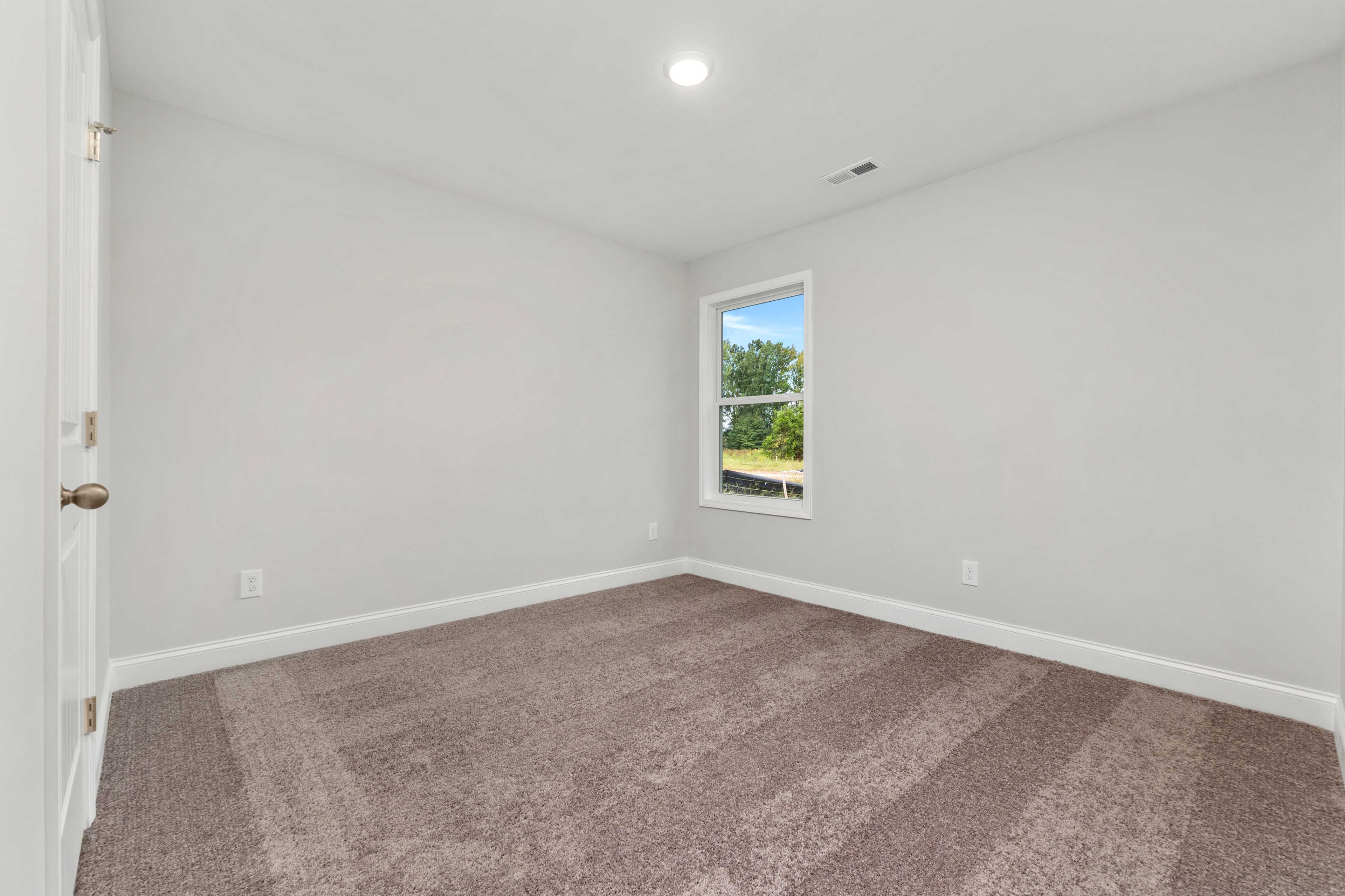 Bright bedroom interior at Collins Lane in Meridianville, Alabama with light gray walls, plush carpet, and large window overlooking greenery